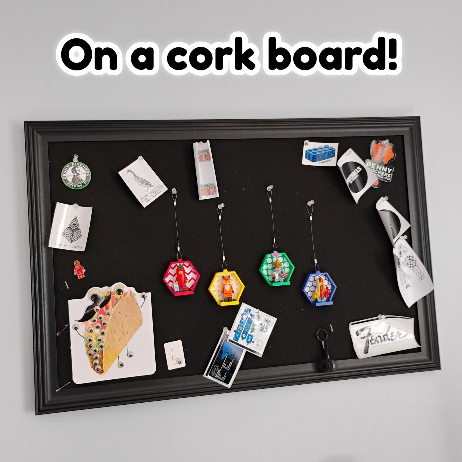 Hanging LEGO® minifigure displays arranged on a cork board with notes and photos for a creative collector display wall.