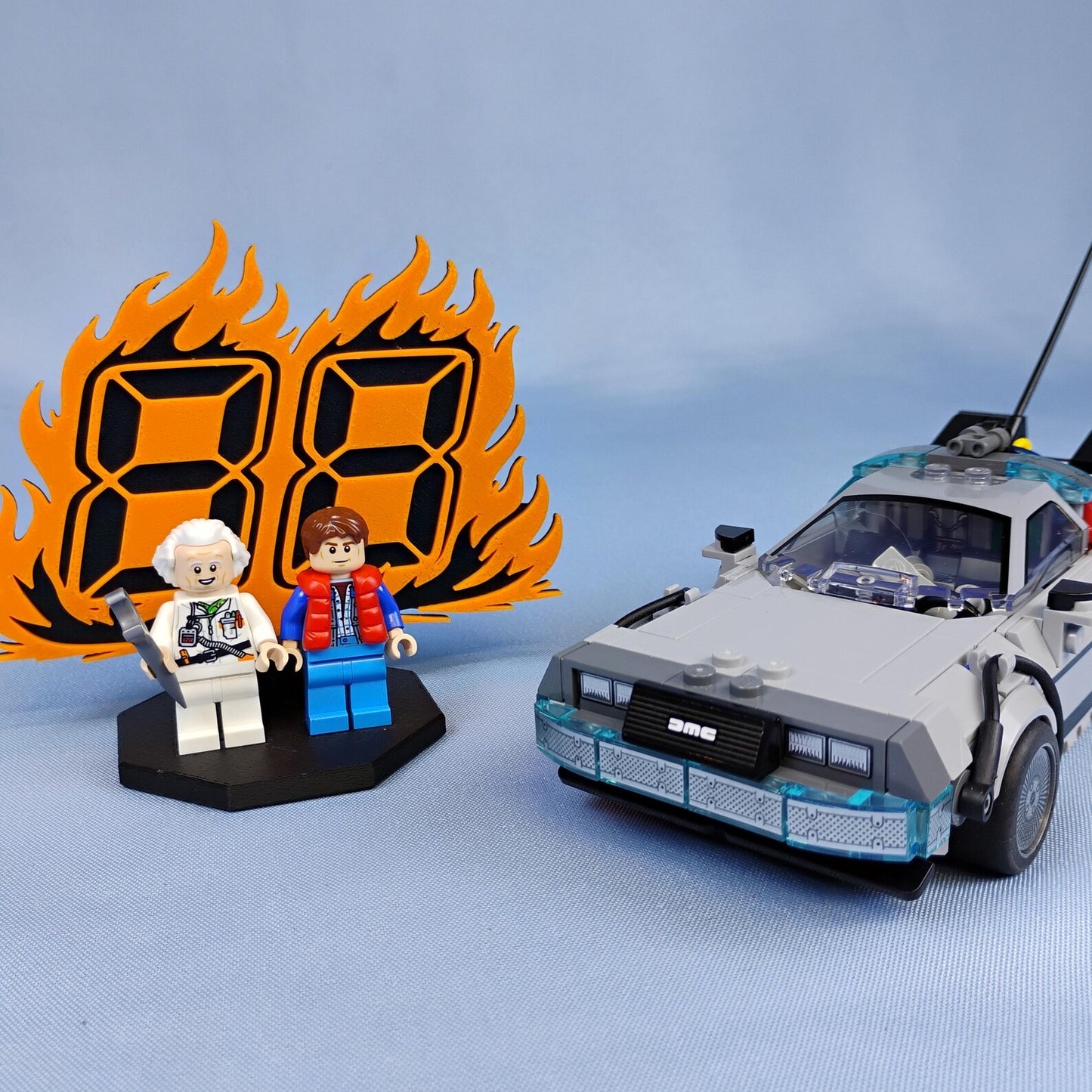 Back to the Future themed display for LEGO® minifigures with orange 88 MPH flame backdrop shown beside a DeLorean time machine build.