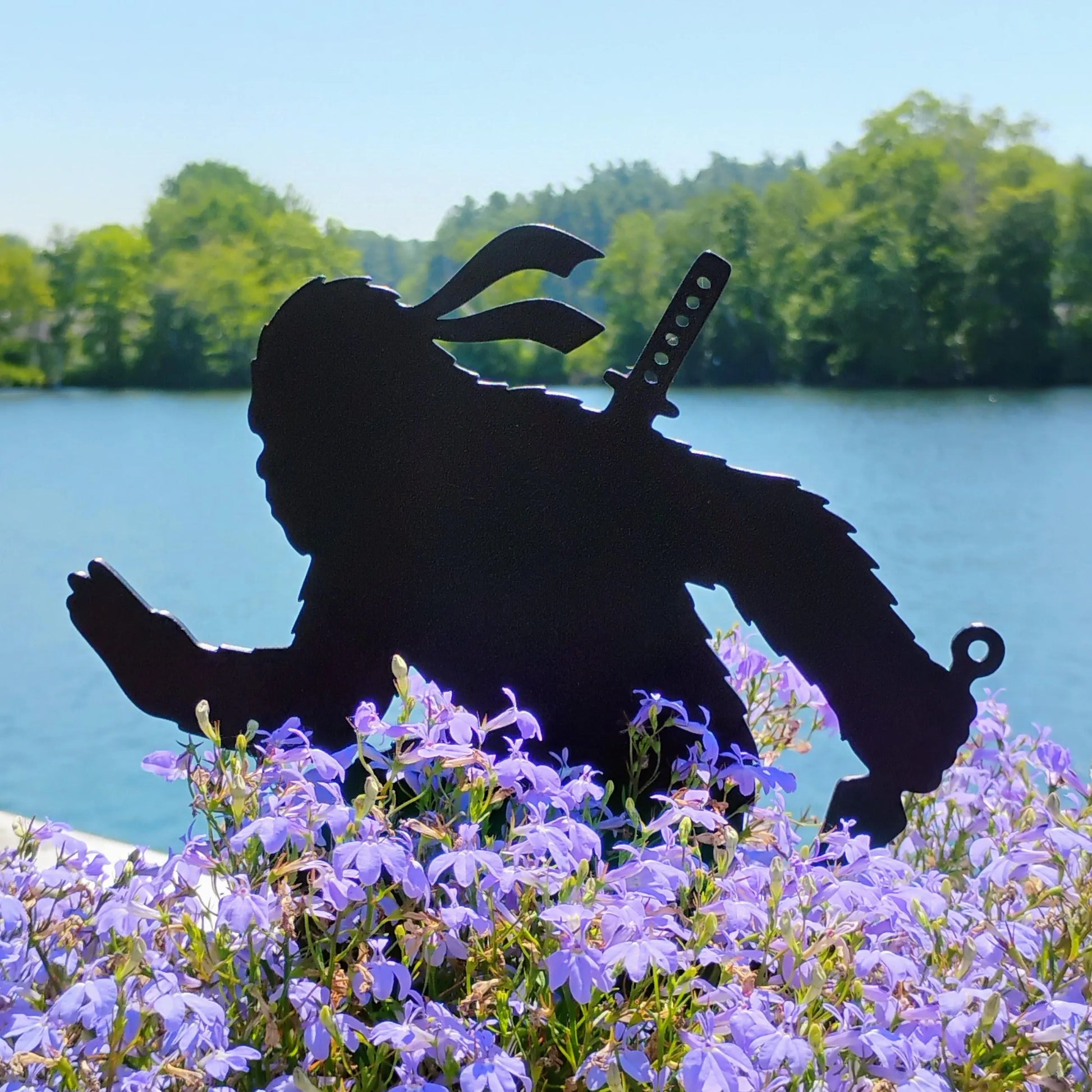 Kunai Creeper Ninja Bigfoot Garden Spike crouching behind purple flowers beside a lake.