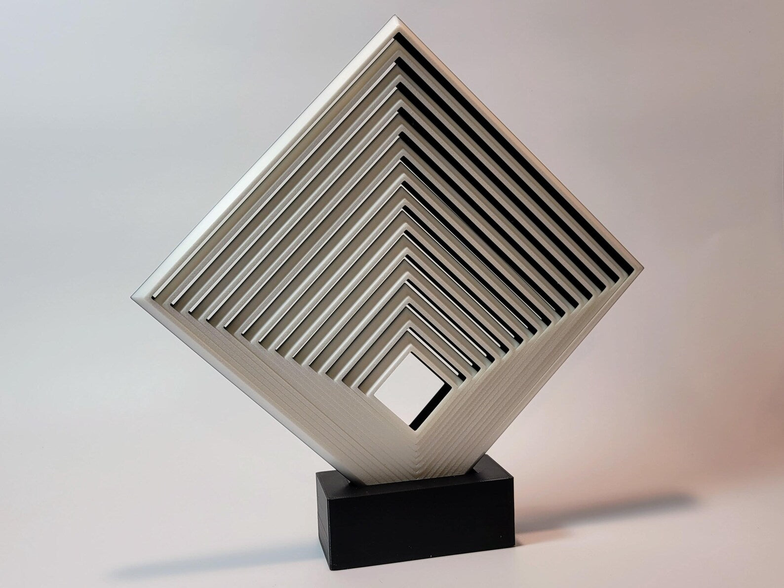 Comically large geometric fidget square displayed upright on a black stand