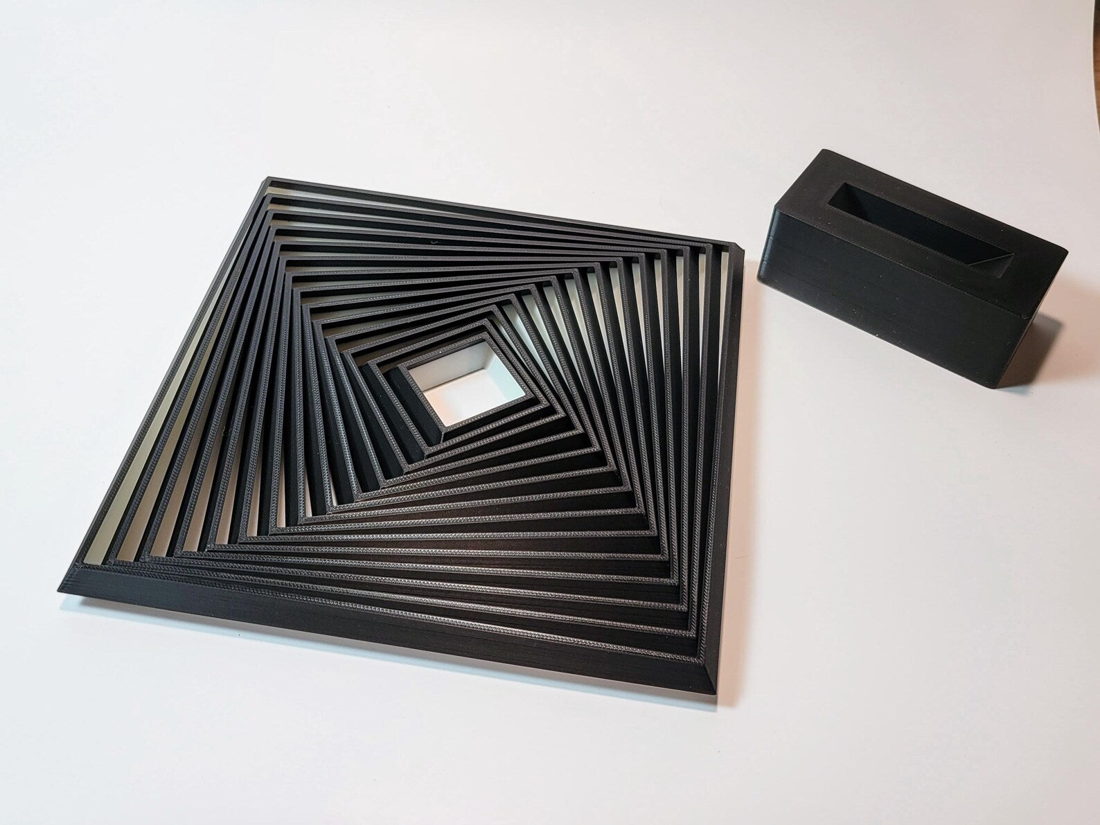 Large layered geometric fidget toy shown at an angle with display stand nearby