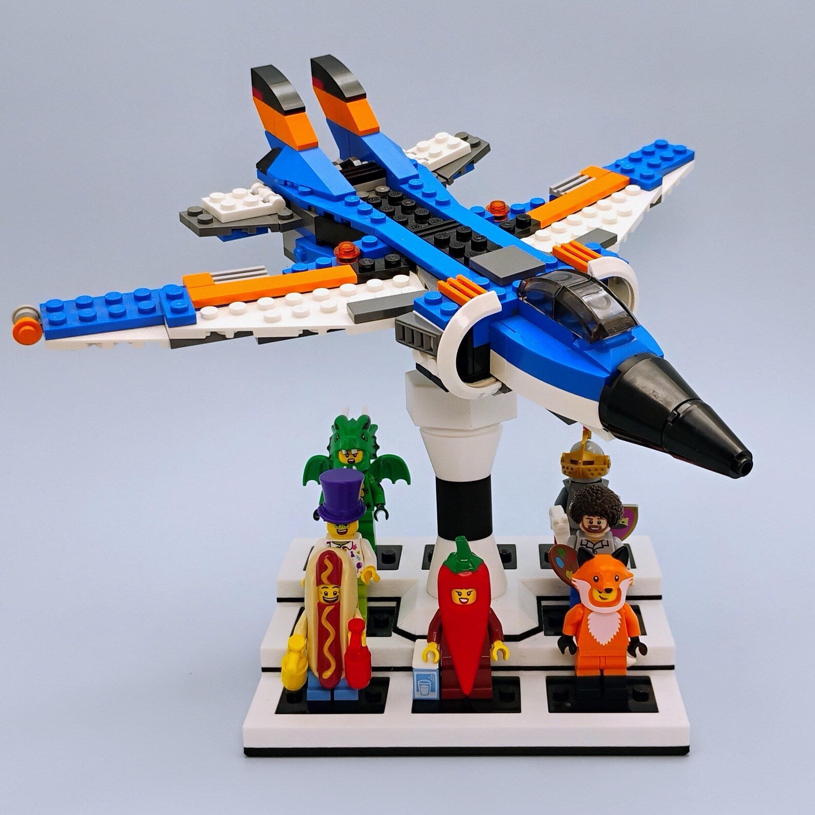 Front angle view of a LEGO® airplane on a white adjustable display stand with minifigures displayed below the model.