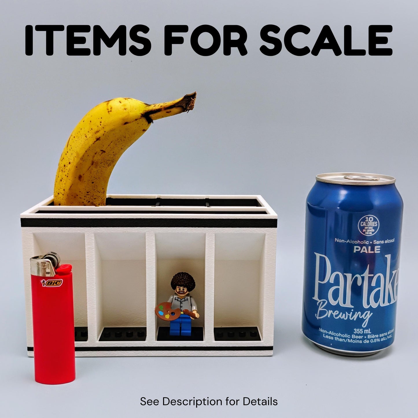 Small model of a jail cell with a banana, toy figure, lighter, and can of Partake Brewing for scale on a gray background.
