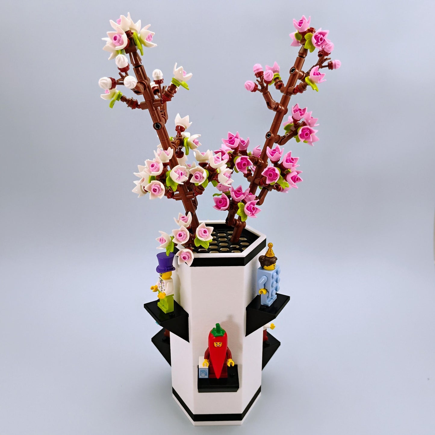 LEGO model of a cherry blossom in a Max Gallows Botanical Vase with LEGO figures displaued around it on a light gray background