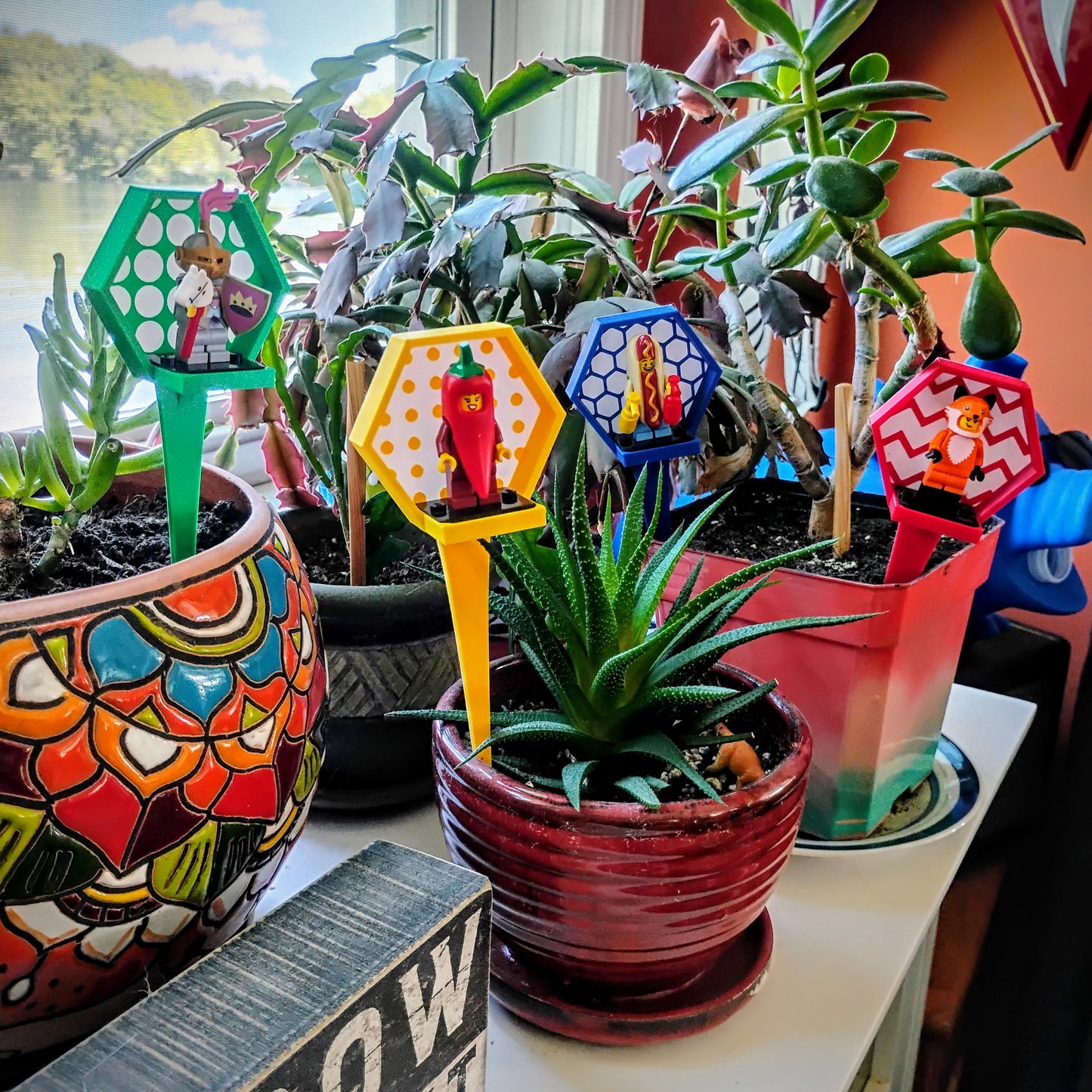 Colorful LEGO® minifigure plant stakes arranged among potted houseplants to create miniature display scenes.