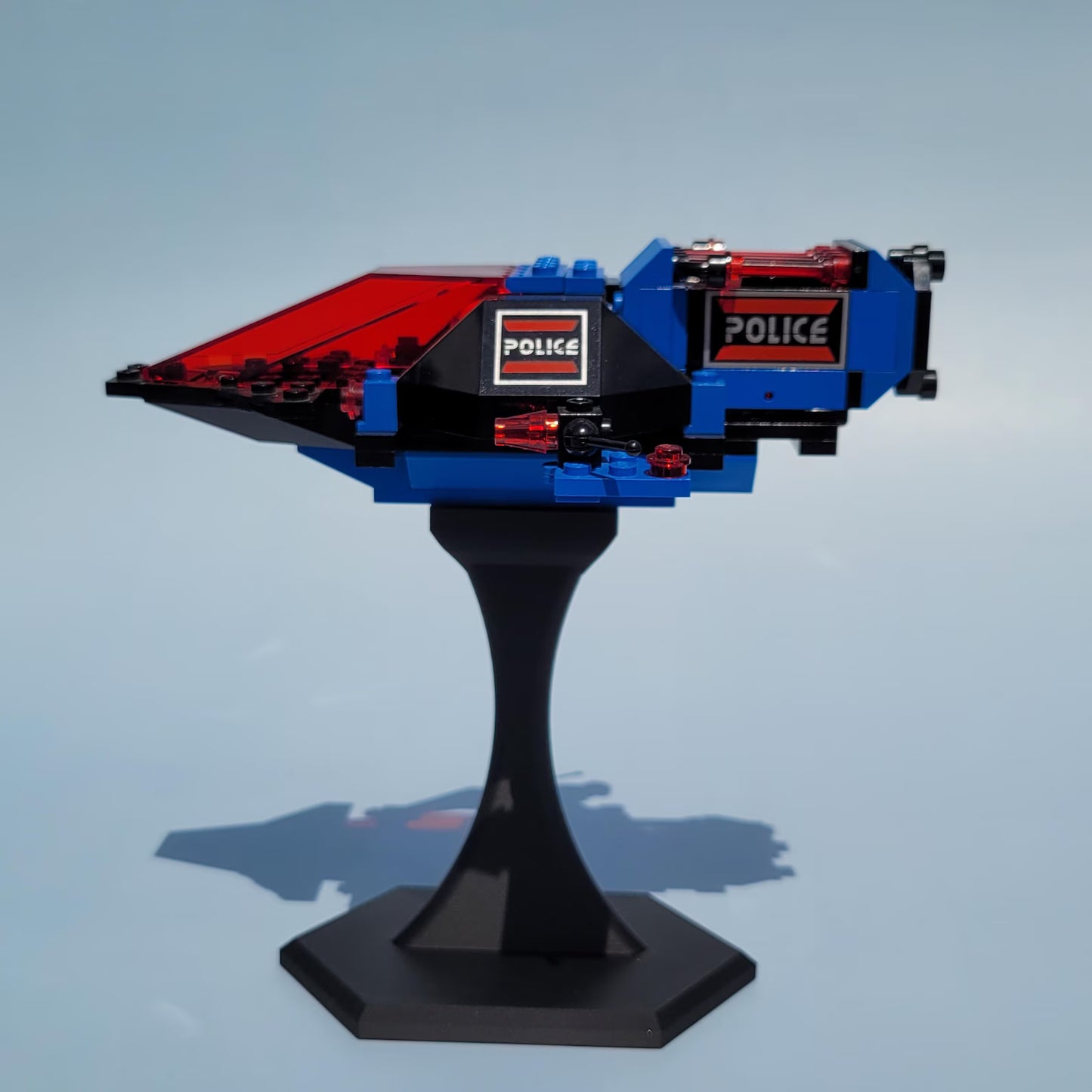 Blue and red LEGO® spaceship displayed on a black riser stand, lifted for a clean desk or shelf display.