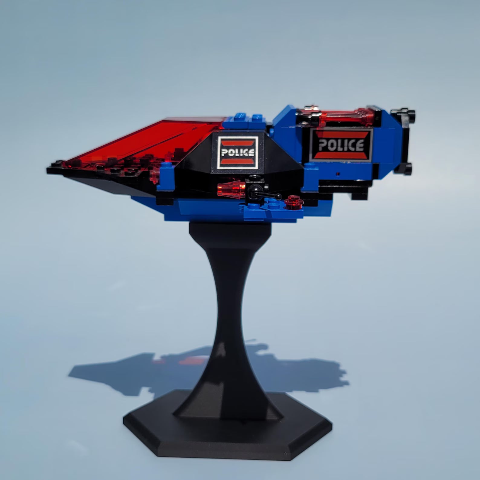 Blue and red LEGO® spaceship displayed on a black riser stand, lifted for a clean desk or shelf display.