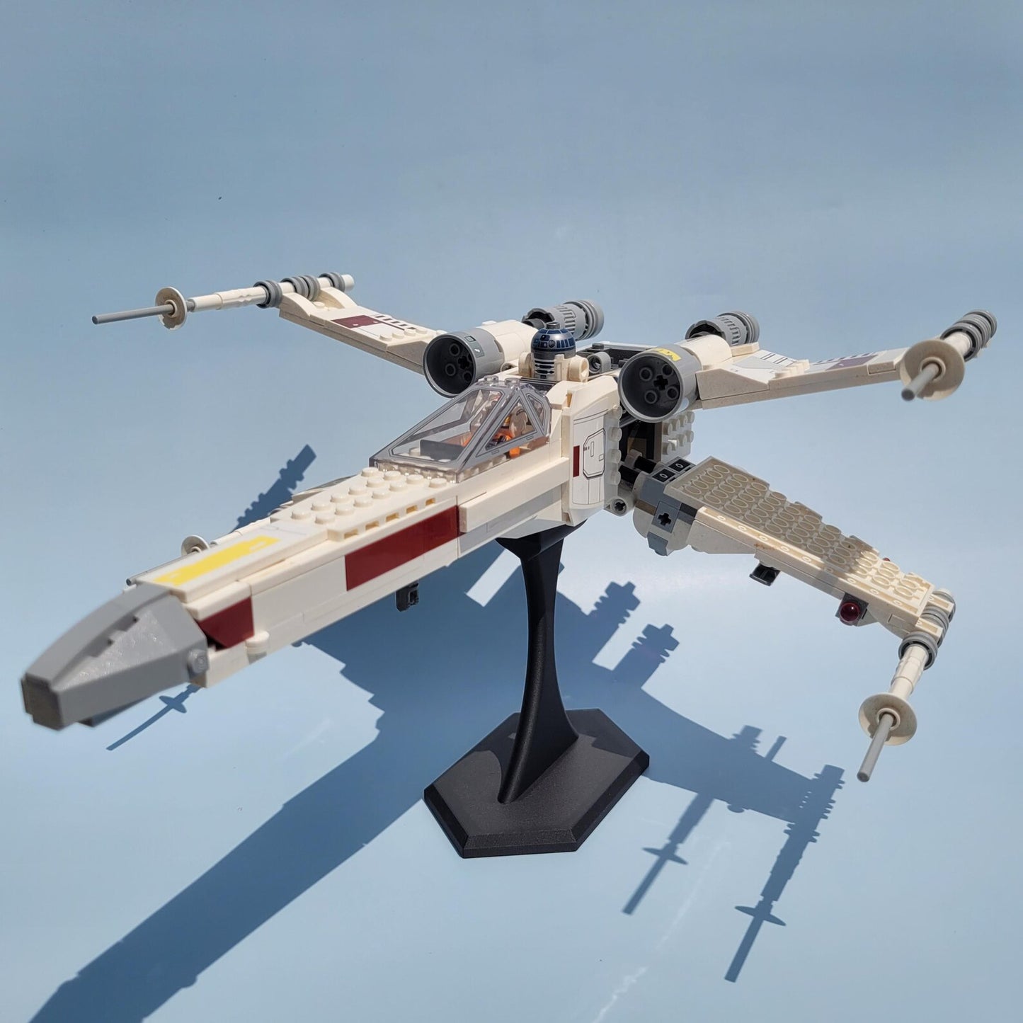 LEGO® X-wing style ship displayed at an angle on a black 4.5 inch stand for dramatic shelf or desk presentation.