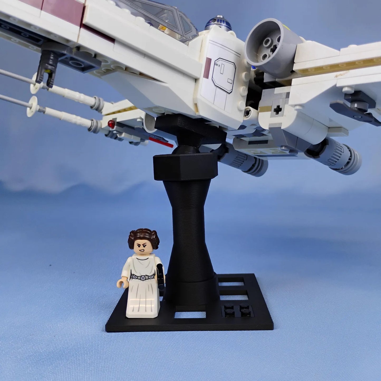 LEGO® X-wing style ship displayed on a black adjustable stand with a minifigure shown on the base for scale and display.