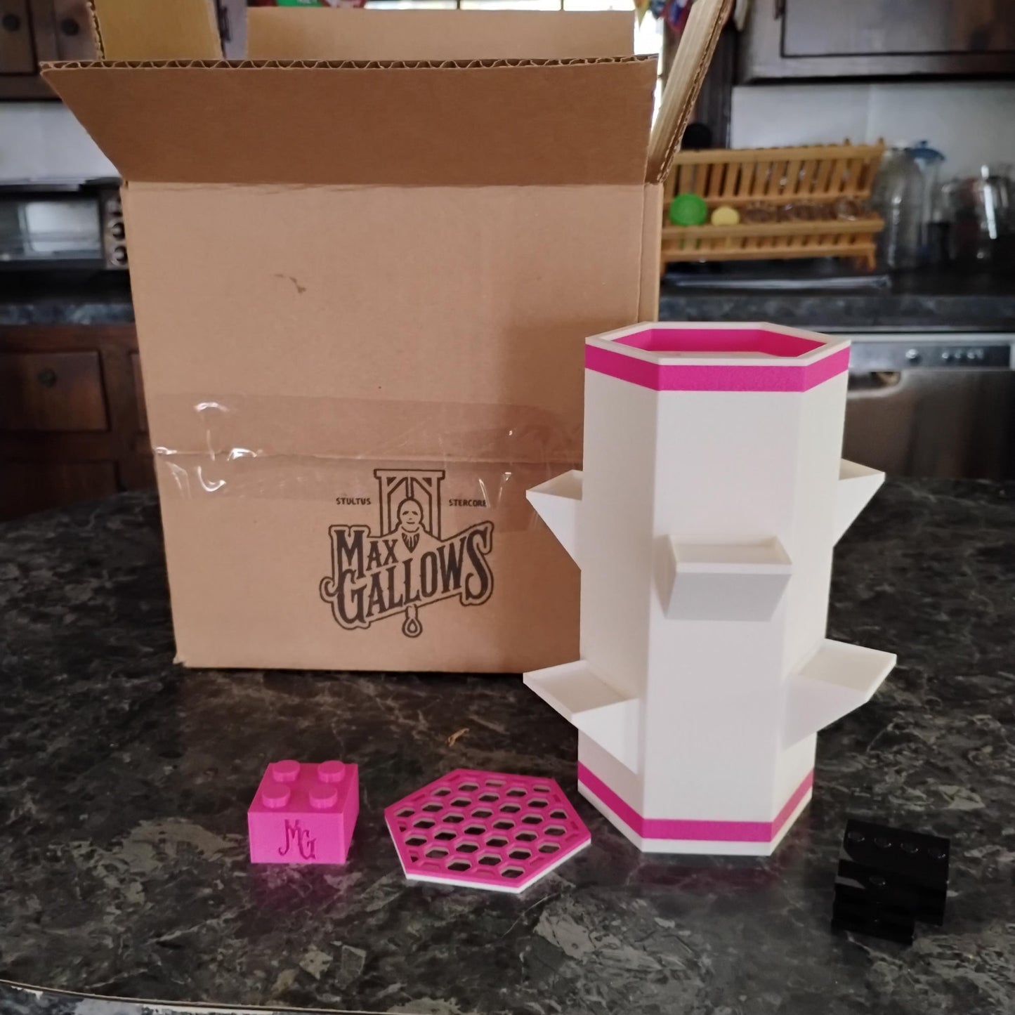 Cardboard box with 'Max Gallows' branding, pink and white geometric vase on a kitchen counter.