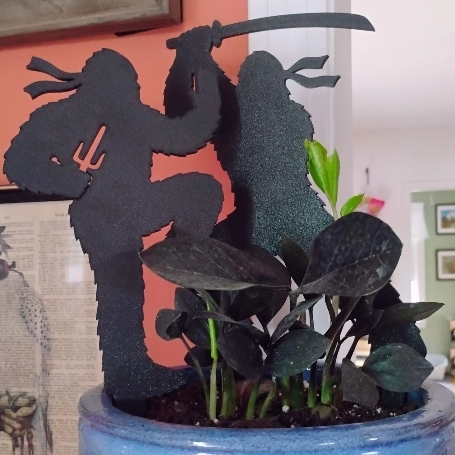 Several Ninja Bigfoot figures displayed indoors around a potted plant with colorful wall art behind them.