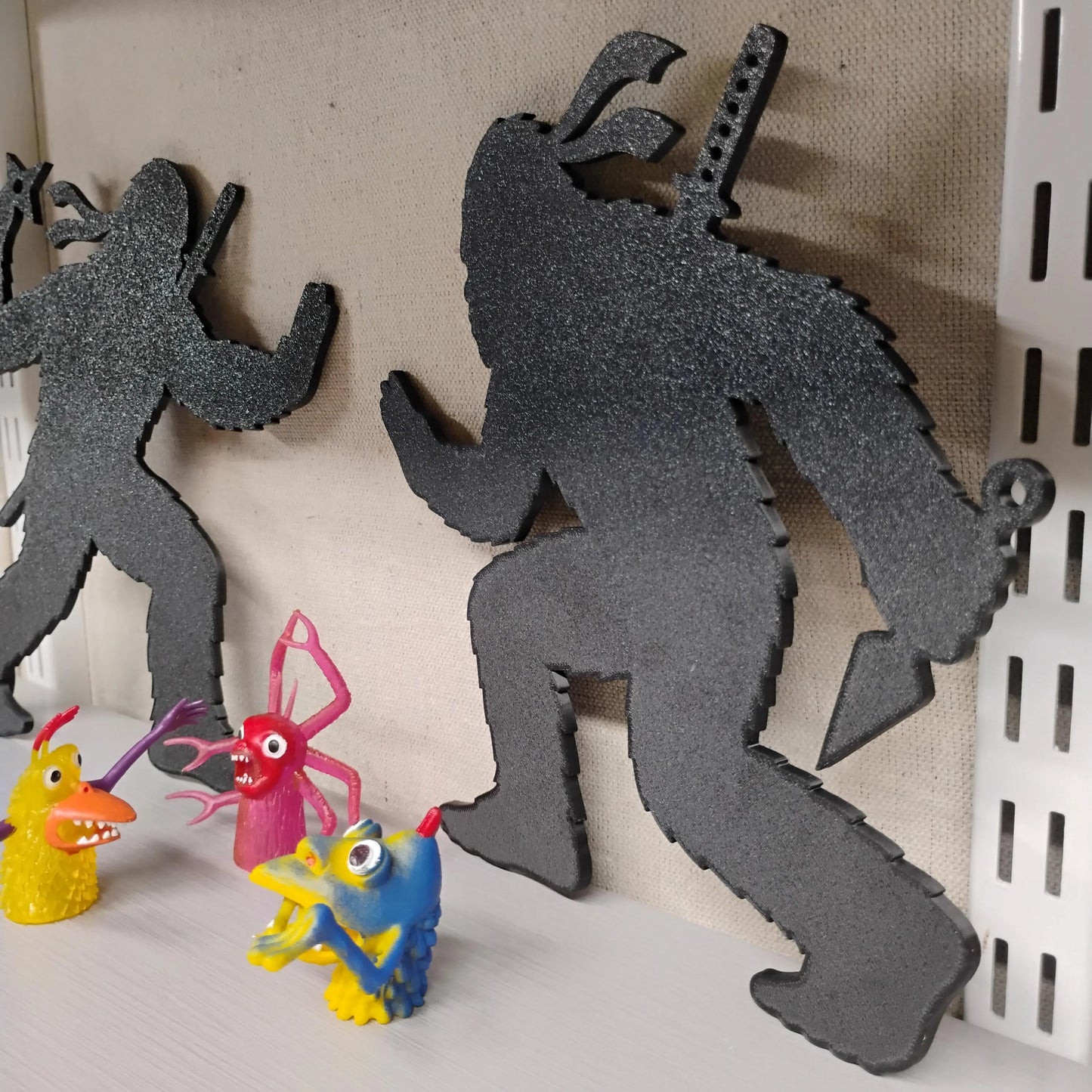 Three black Ninja Bigfoot figures displayed indoors on a shelf with colorful toy figures for scale.