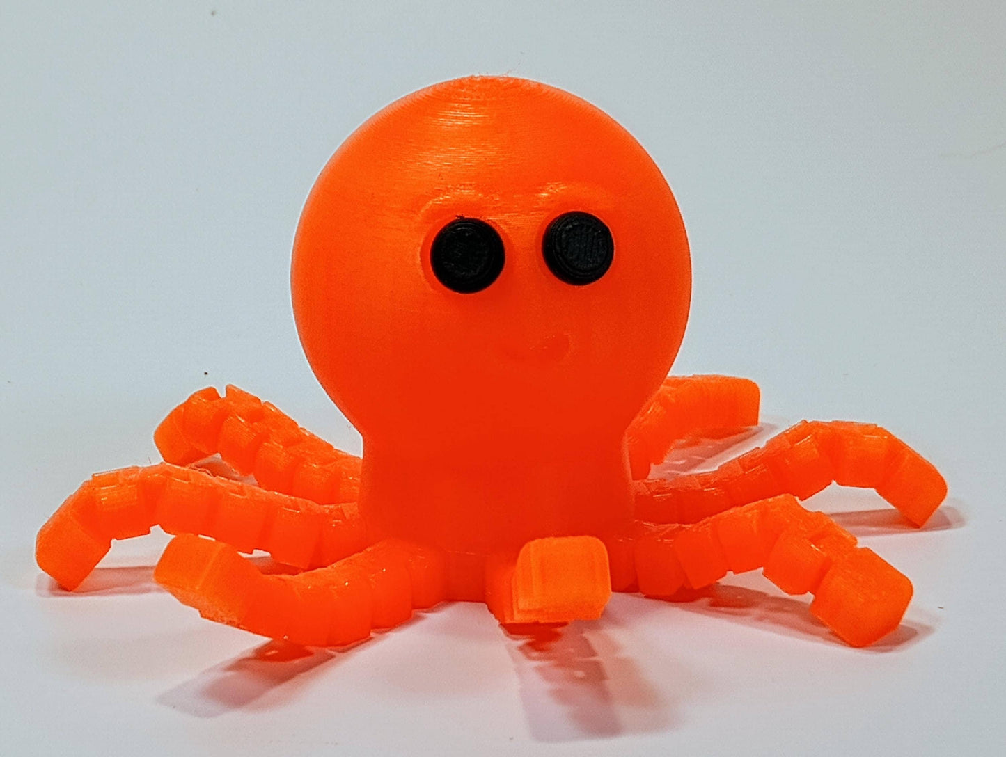 Orange flexi octopus figurine with black eyes, bendy articulated legs, and cute desk buddy style shown on a white background.