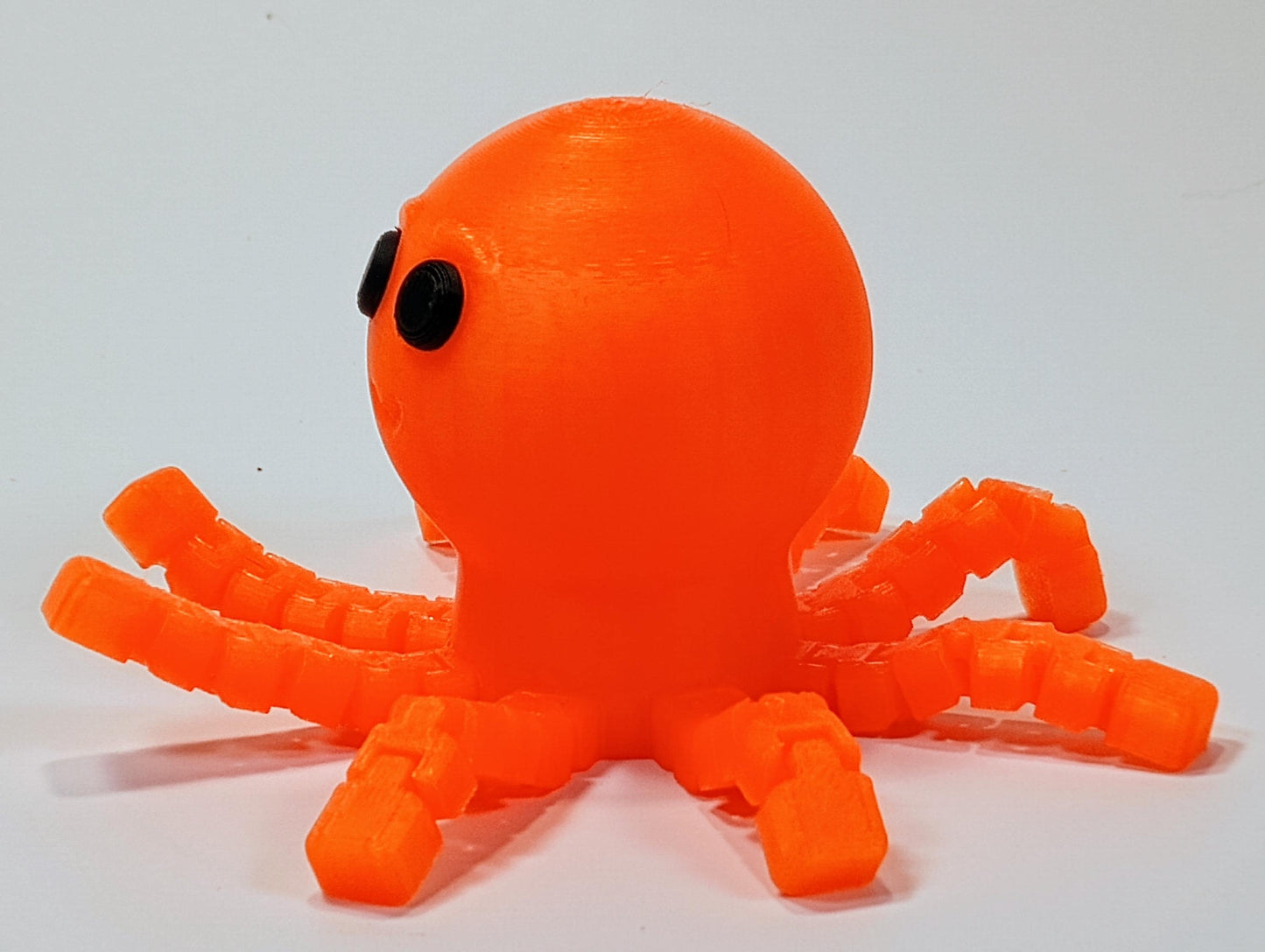 Side view of an orange flexi octopus figurine showing the rounded head, black eyes, and articulated wiggly legs.