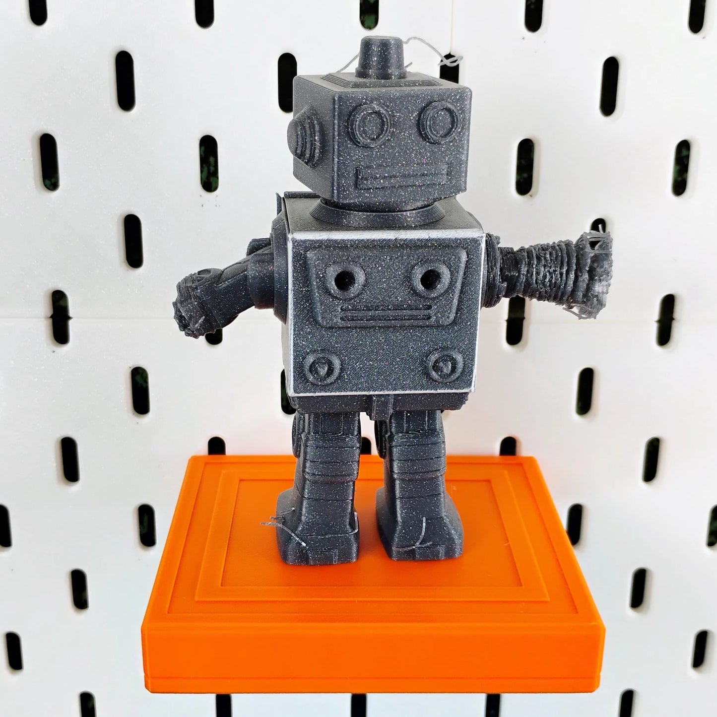 Orange SKADIS floating shelf displaying a gray robot figure