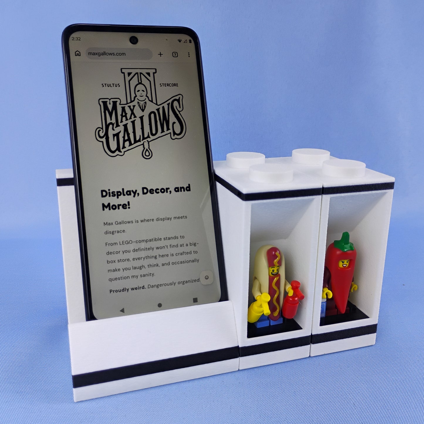 White modular phone stand connected to a two-minifigure display brick with LEGO® figures beside the smartphone.