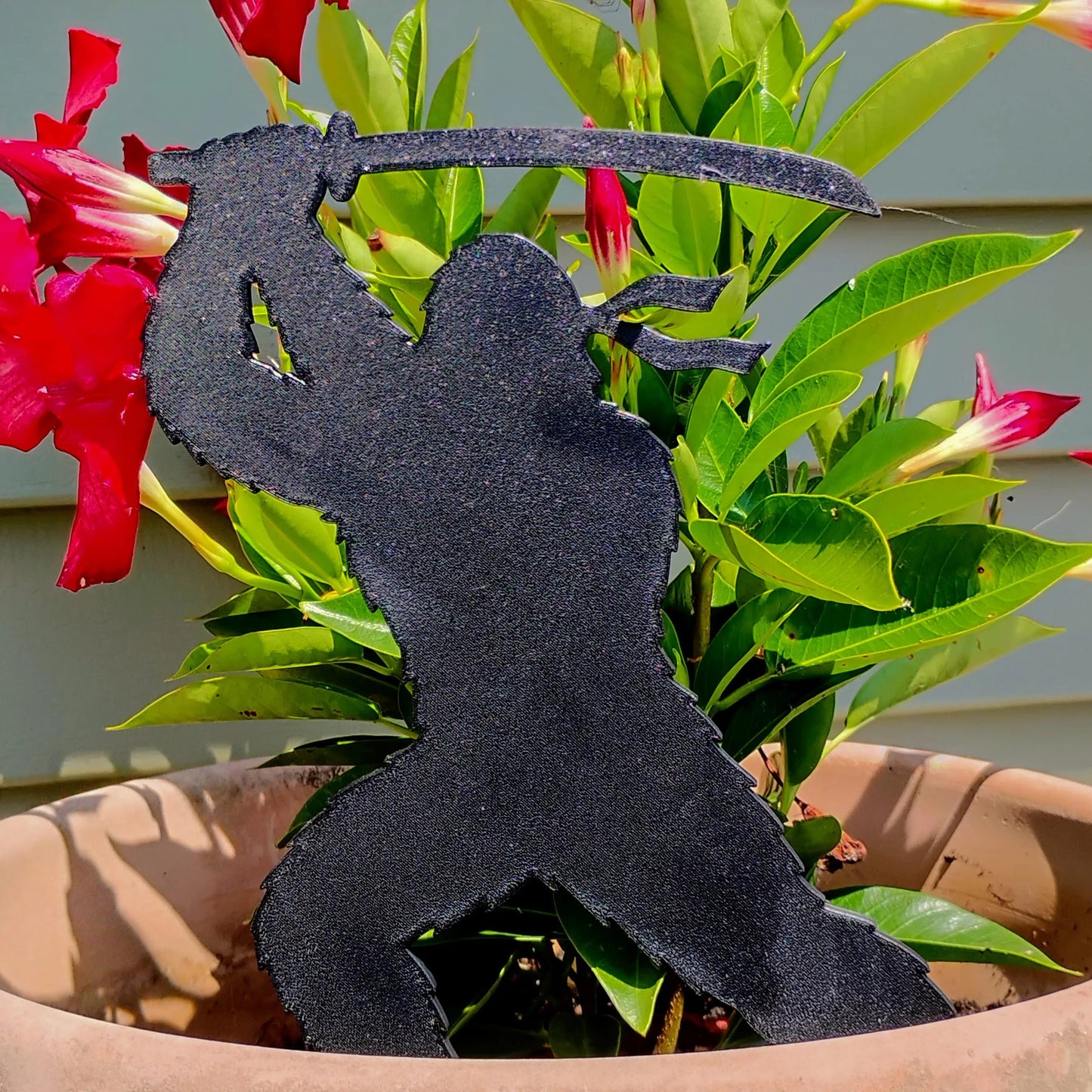 The Pointy One Ninja Bigfoot Garden Spike displayed in a flowerpot surrounded by red and green plants.