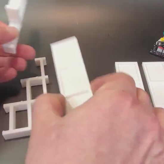 Hands assembling a tiered display stand for LEGO® minifigures by attaching the support pieces.