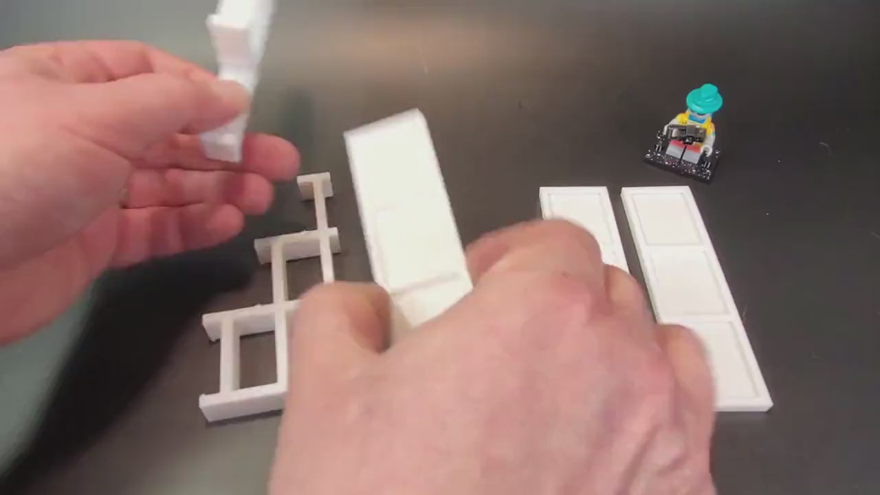 Hands assembling a tiered display stand for LEGO® minifigures by attaching the support pieces.