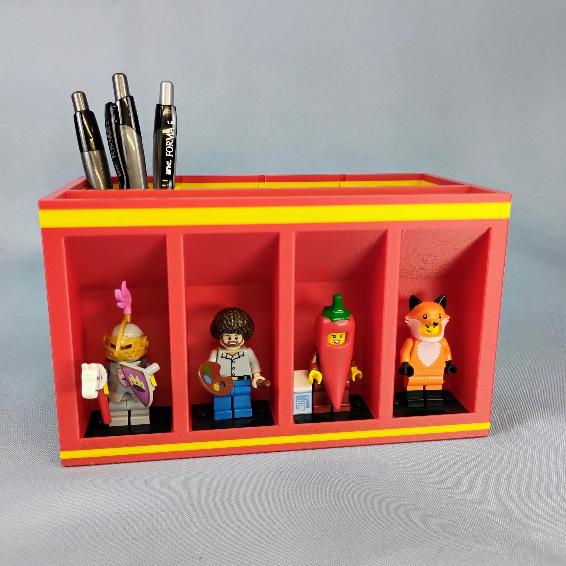 Red and yellow desk organizer with lego minifigures and pens on a gray background