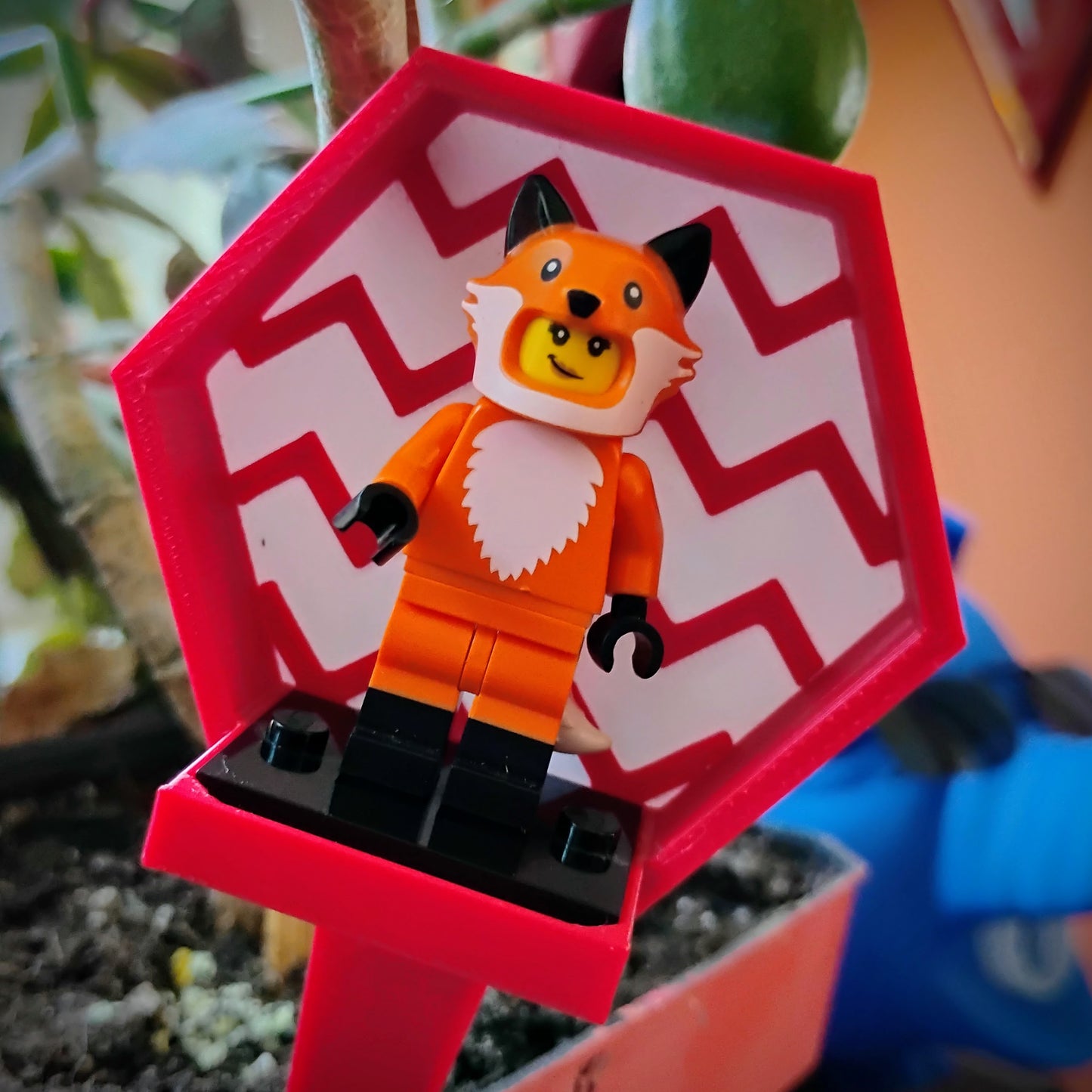 Red zigzag LEGO® minifigure plant stake displayed in a flowerpot with a fox-costume minifigure.