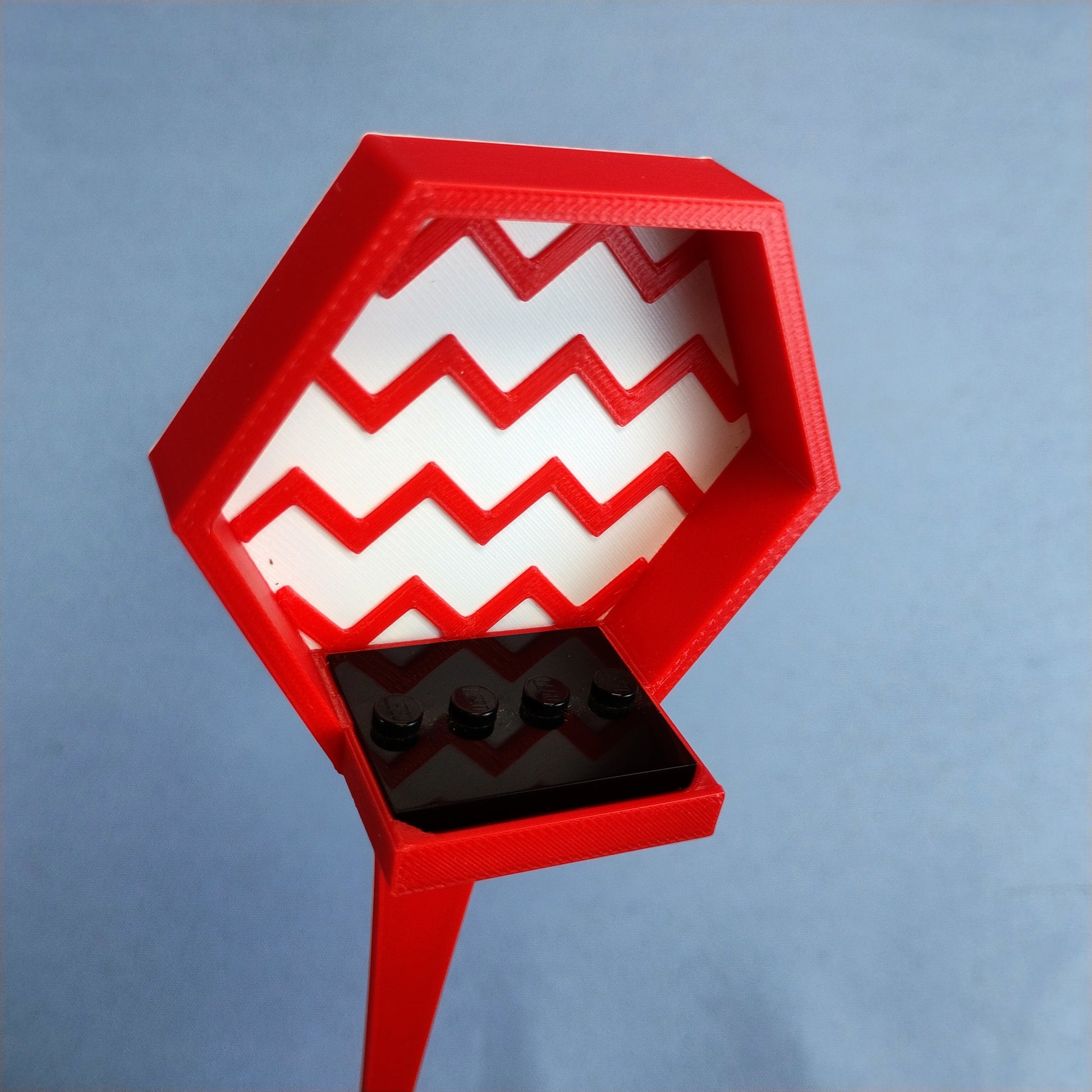 Close-up of a red LEGO® minifigure plant stake display with a white zigzag background and black minifigure plate.