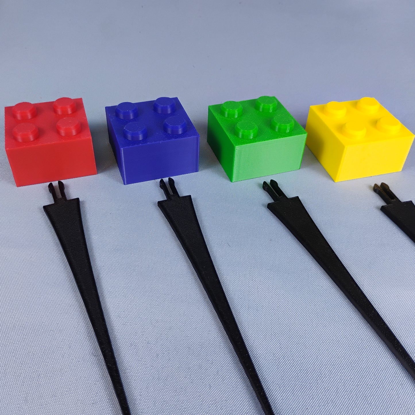 Four building brick plant stakes in red, blue, green and yellow displayed on a neutral background.