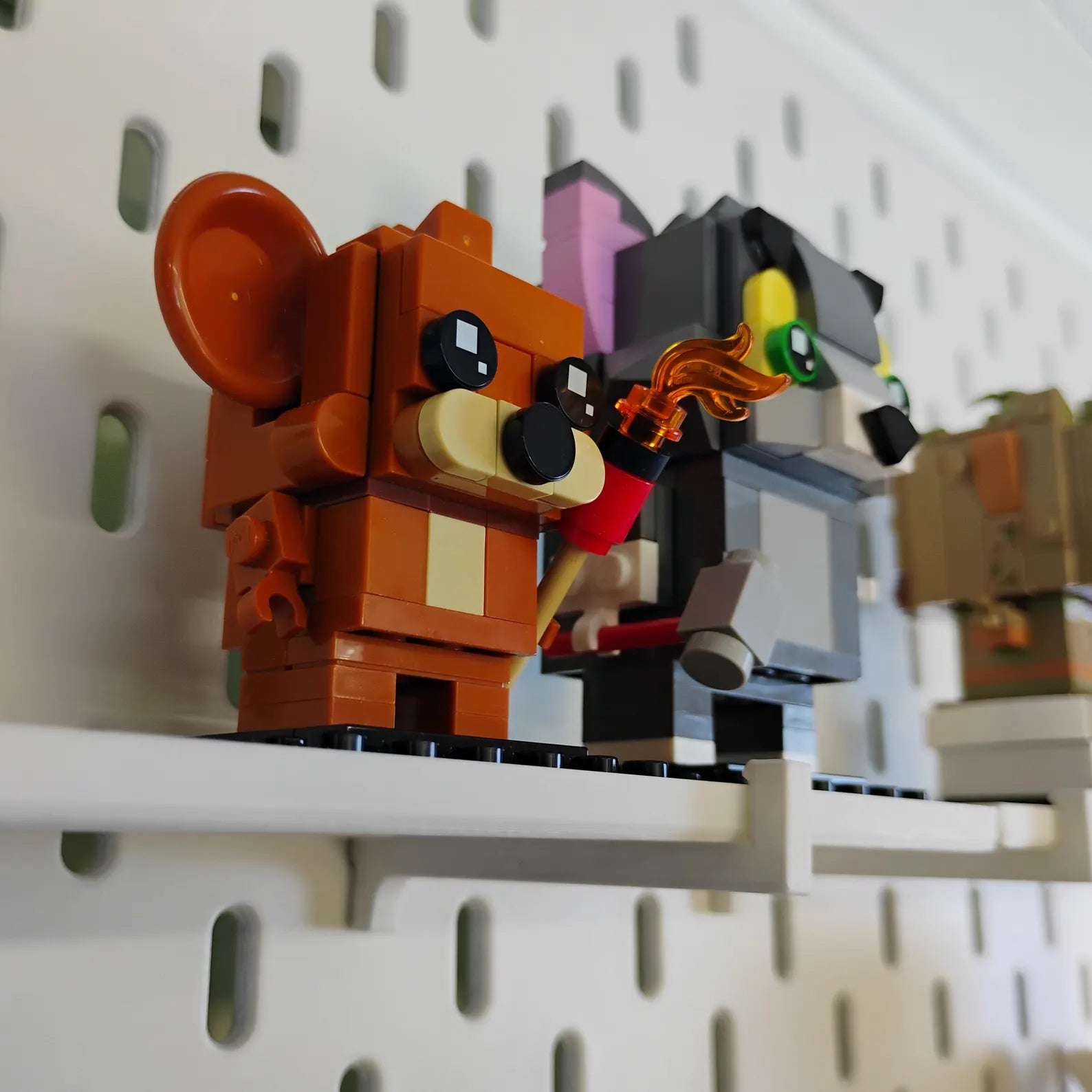 Side view of SKÅDIS-compatible BrickHeadz™ shelves showing figures displayed on black shelves mounted to an IKEA pegboard.