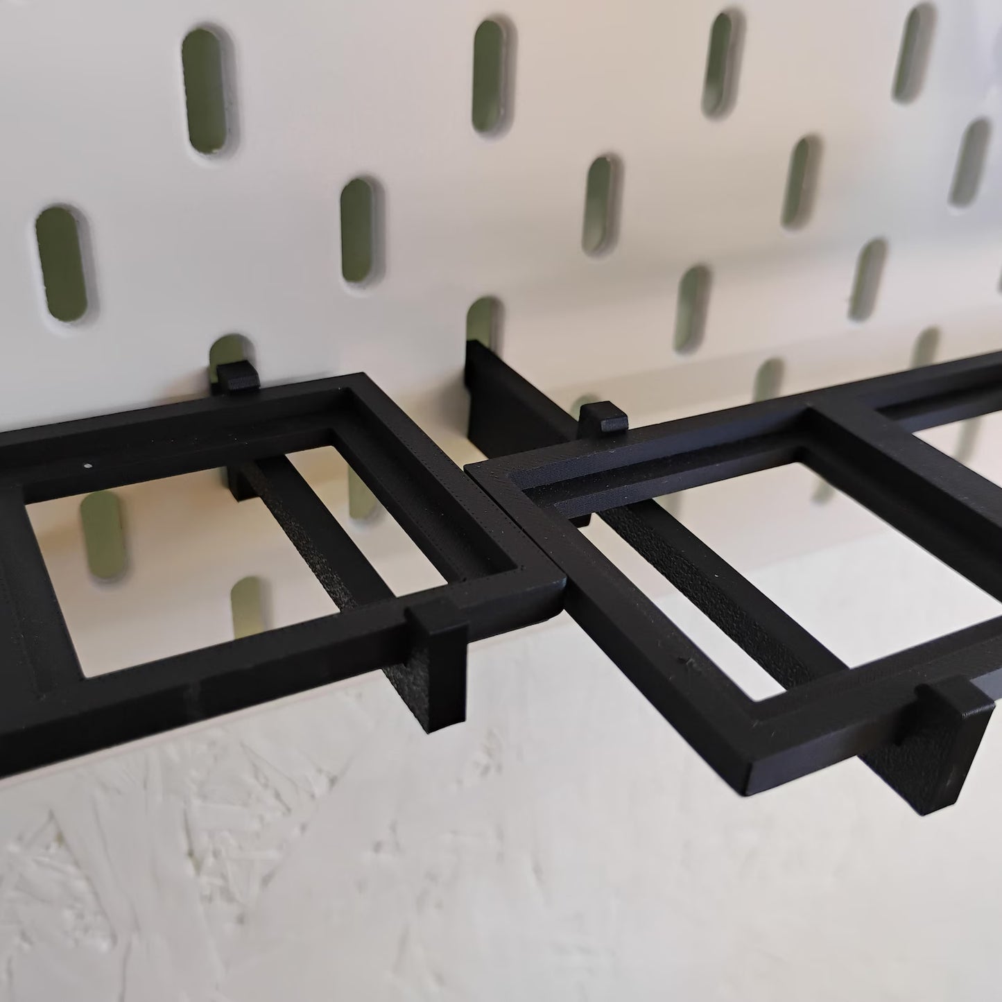Close-up of black SKÅDIS-compatible shelf support pins and shelf frame mounted into an IKEA pegboard.