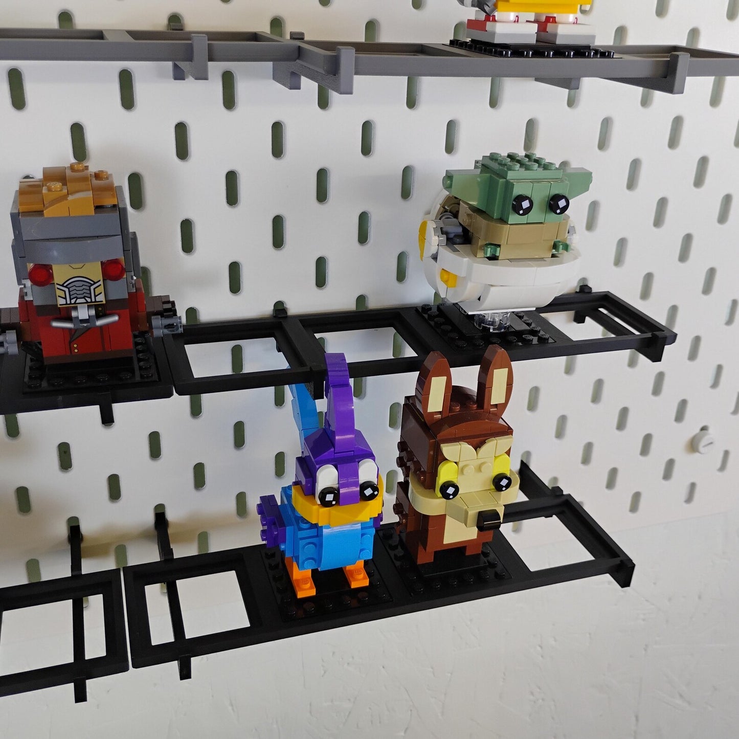 SKÅDIS-compatible BrickHeadz™ shelves displaying figures with rear overhangs, using deeper shelf spacing on an IKEA pegboard.