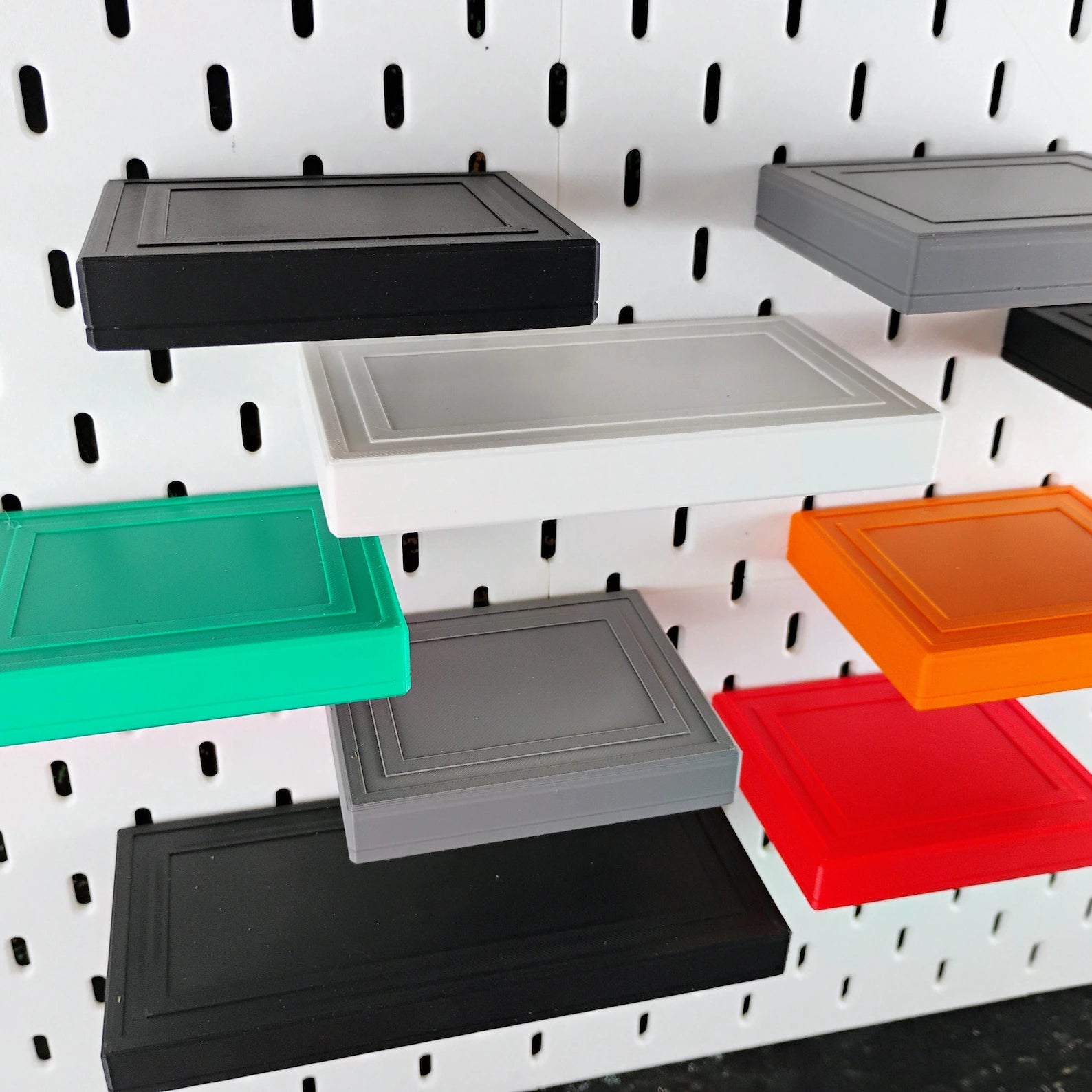 Assorted SKADIS floating shelves in black, white, gray, teal, and orange mounted on pegboard