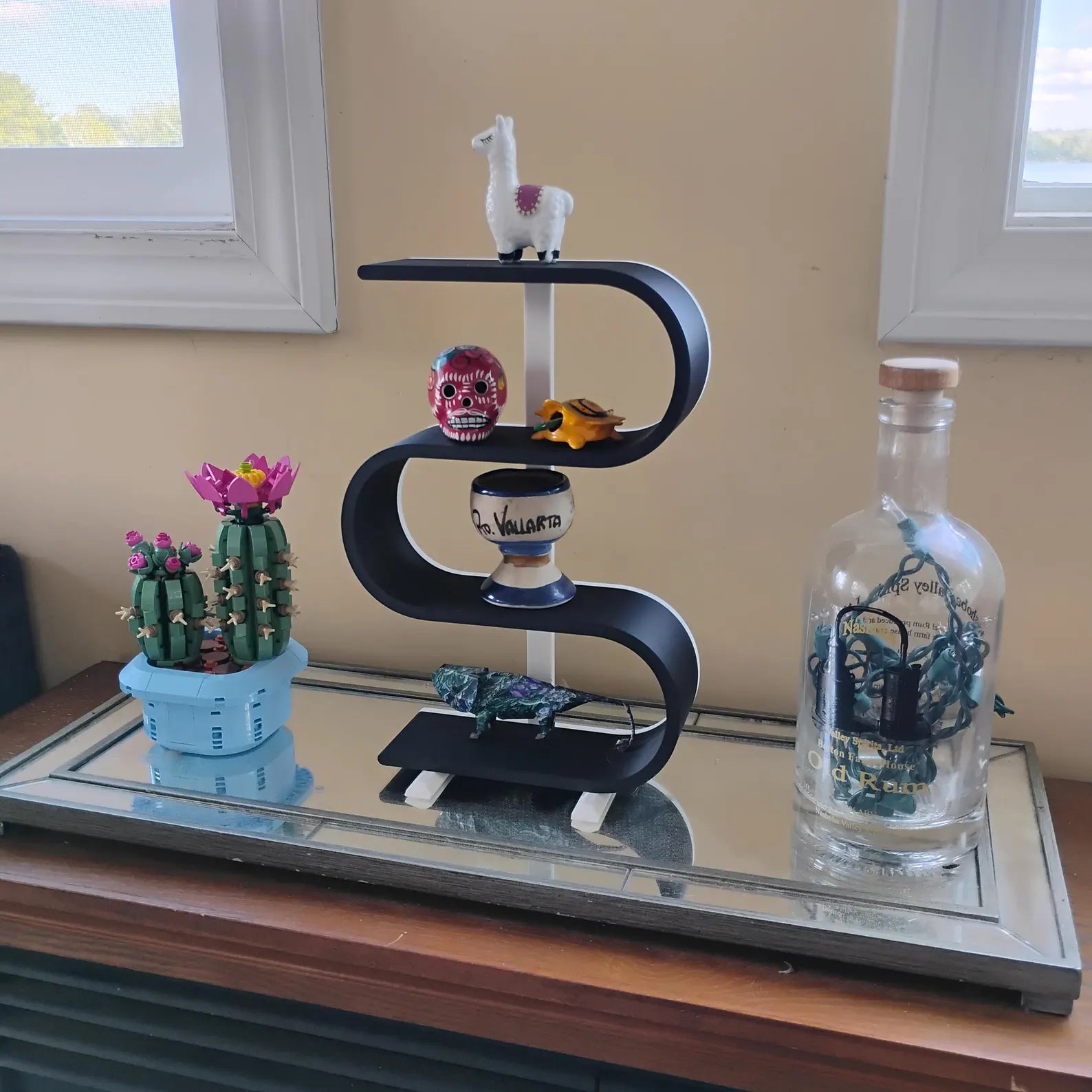 Black squiggly display shelf arranged on a dresser with small figures, a skeleton decoration, plants, flowers, and decorative bottles for a playful home decor display.