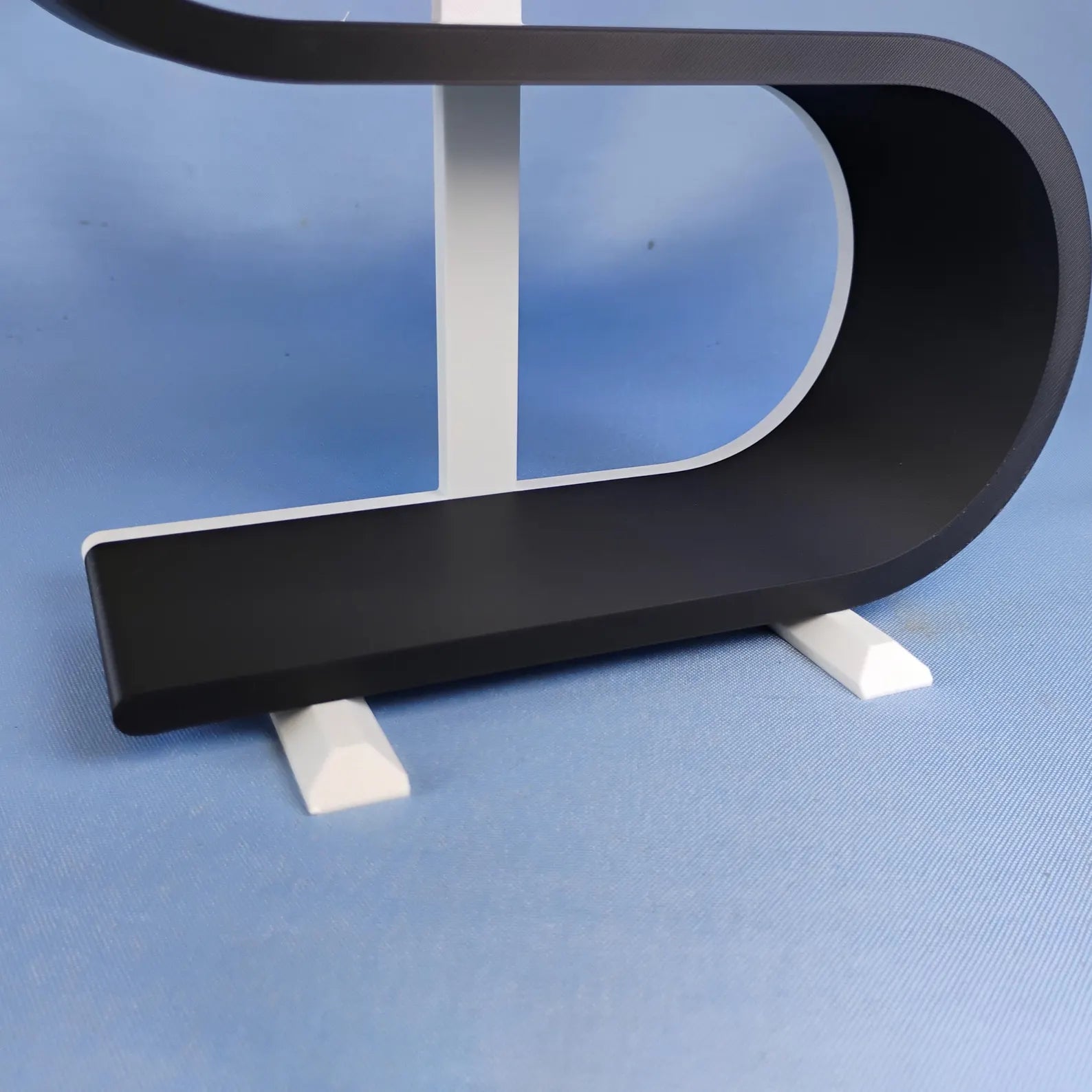 Close-up of the removable white feet attached beneath a black squiggly display shelf for stable freestanding use on a desk, dresser, or tabletop.