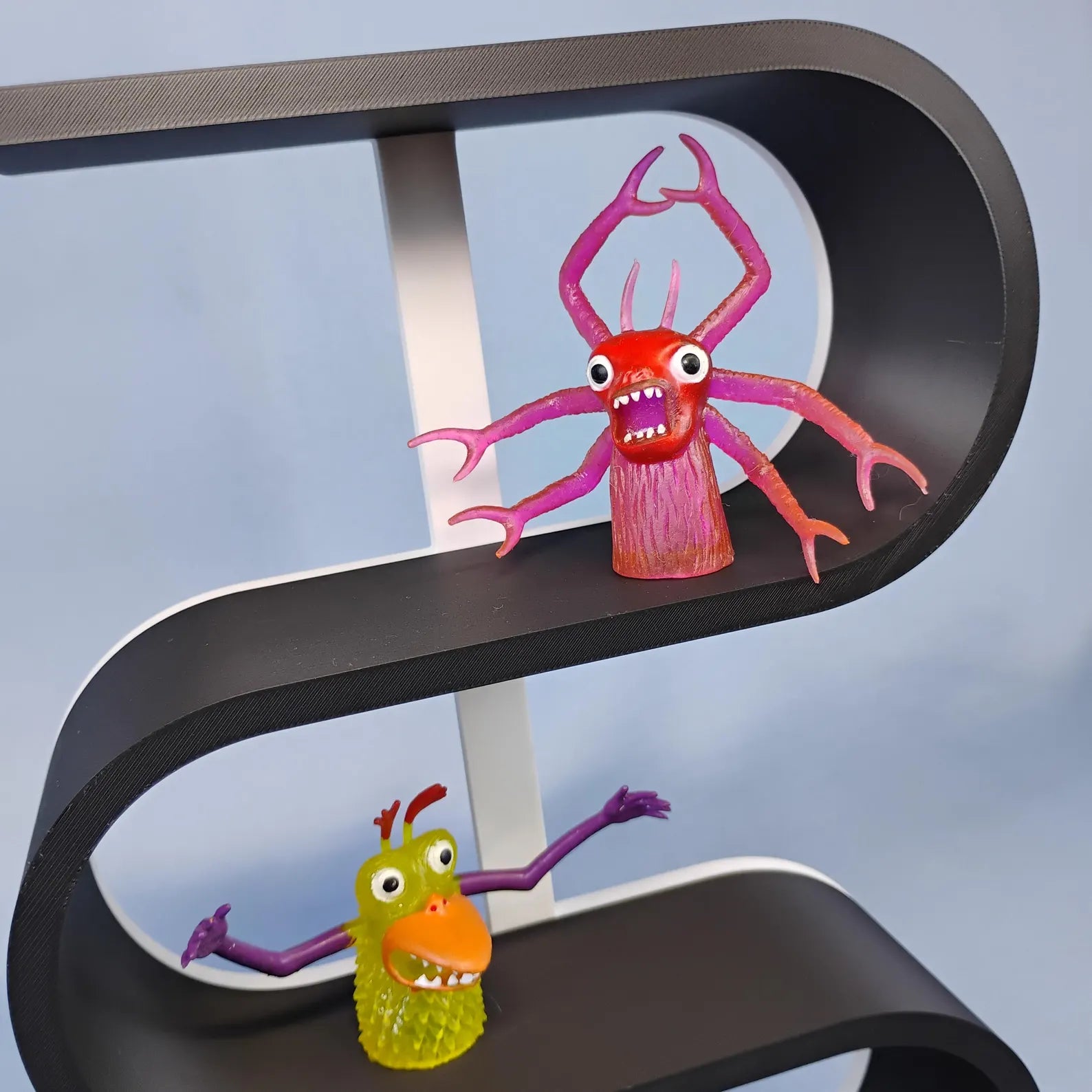 Close-up of the curved levels on a black squiggly display shelf with a white center support, holding pink and orange miniature monster figures.