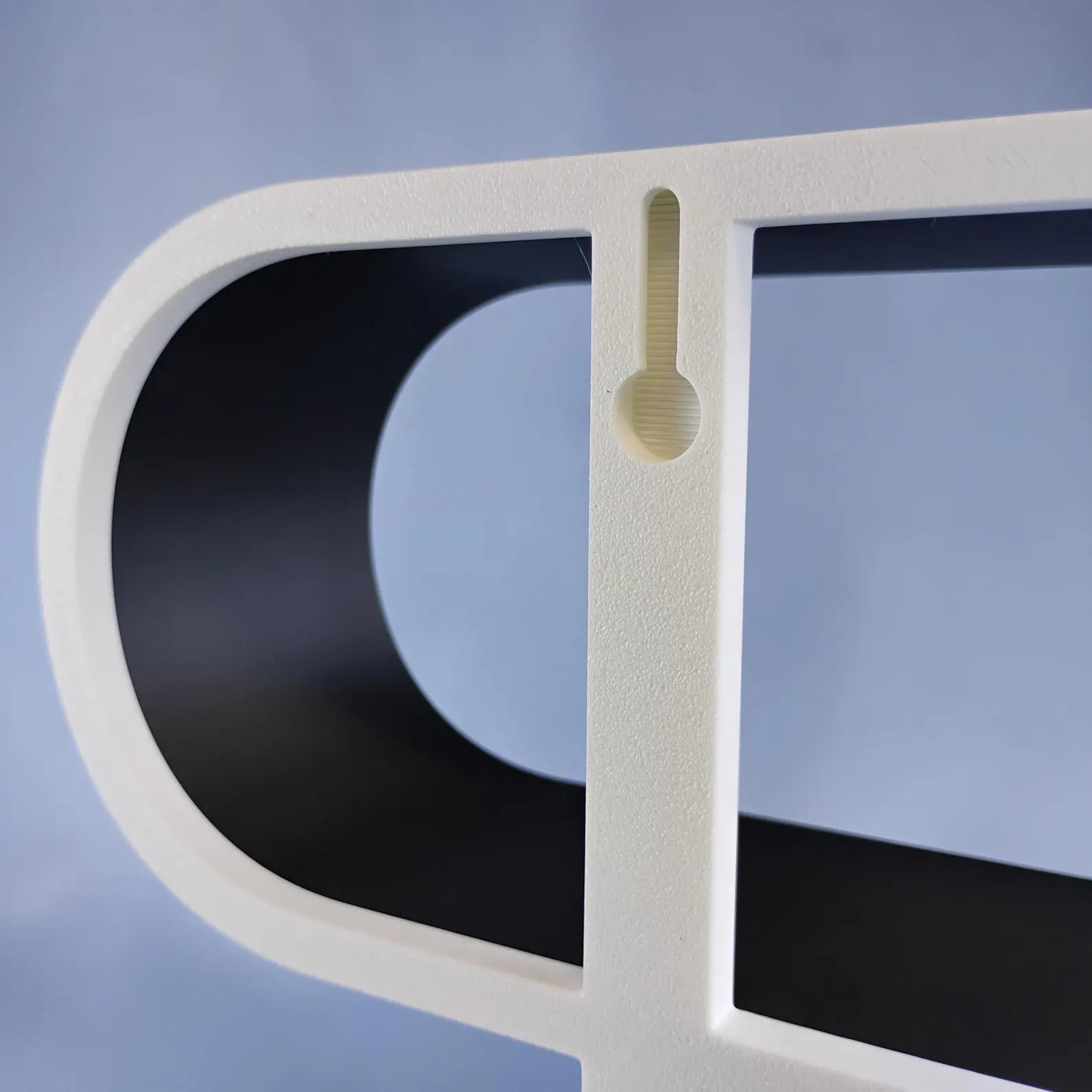 Close-up of the built-in wall-mount opening on the back of a squiggly display shelf, allowing the tabletop shelf to be converted into a hanging wall display.