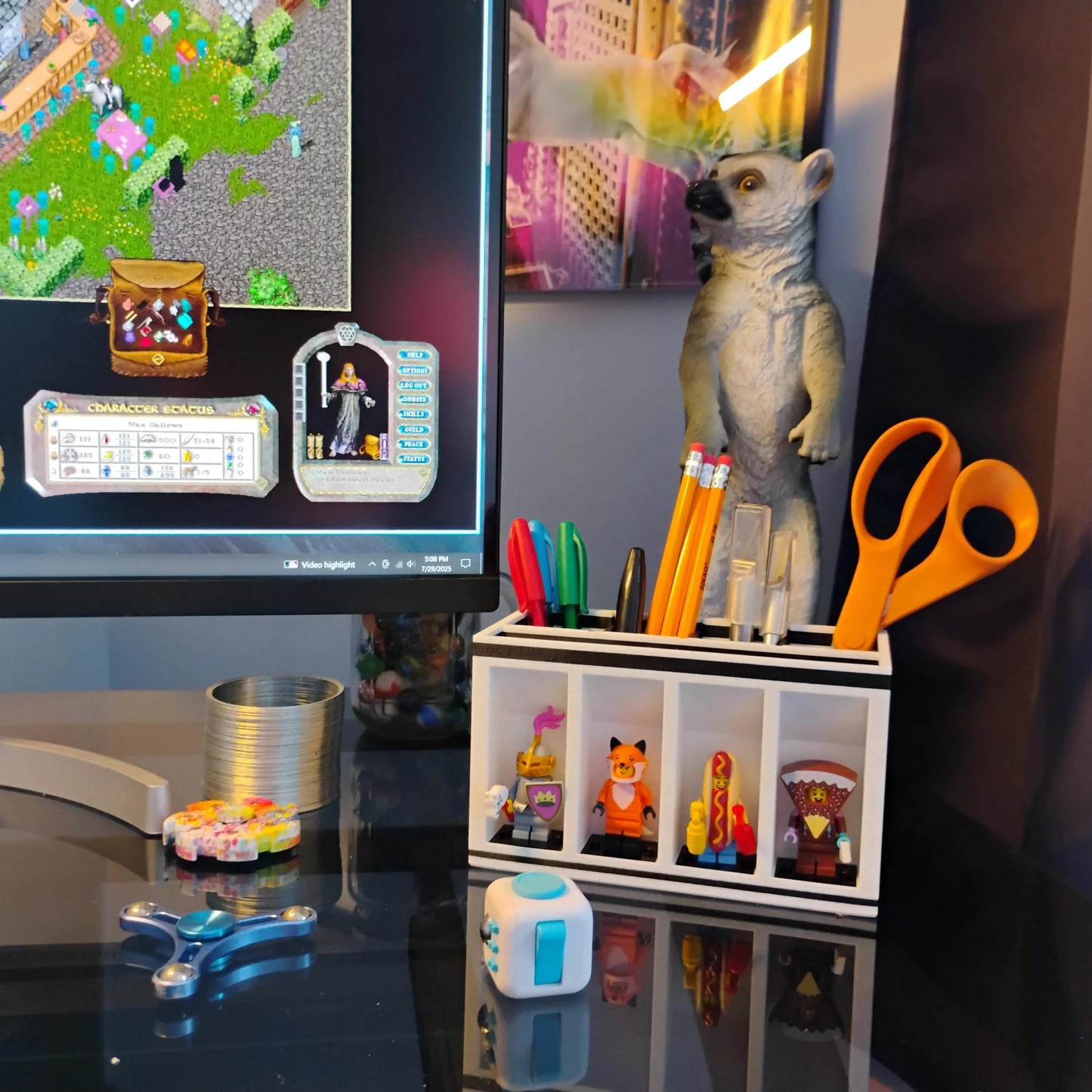 Desk setup with computer monitor, stationery items, a LEGO Minifigure Desk Organizer and a toy lemur.