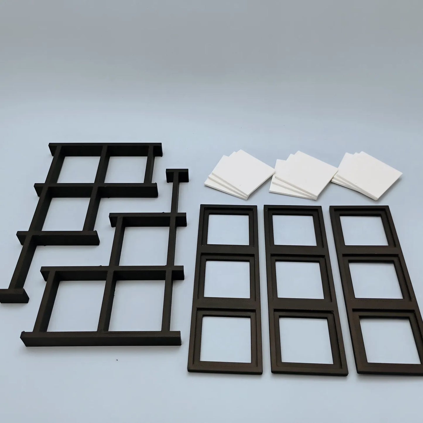 Tiered display stand shown disassembled with black frame pieces and removable white tiles for easy cleaning and color swapping.