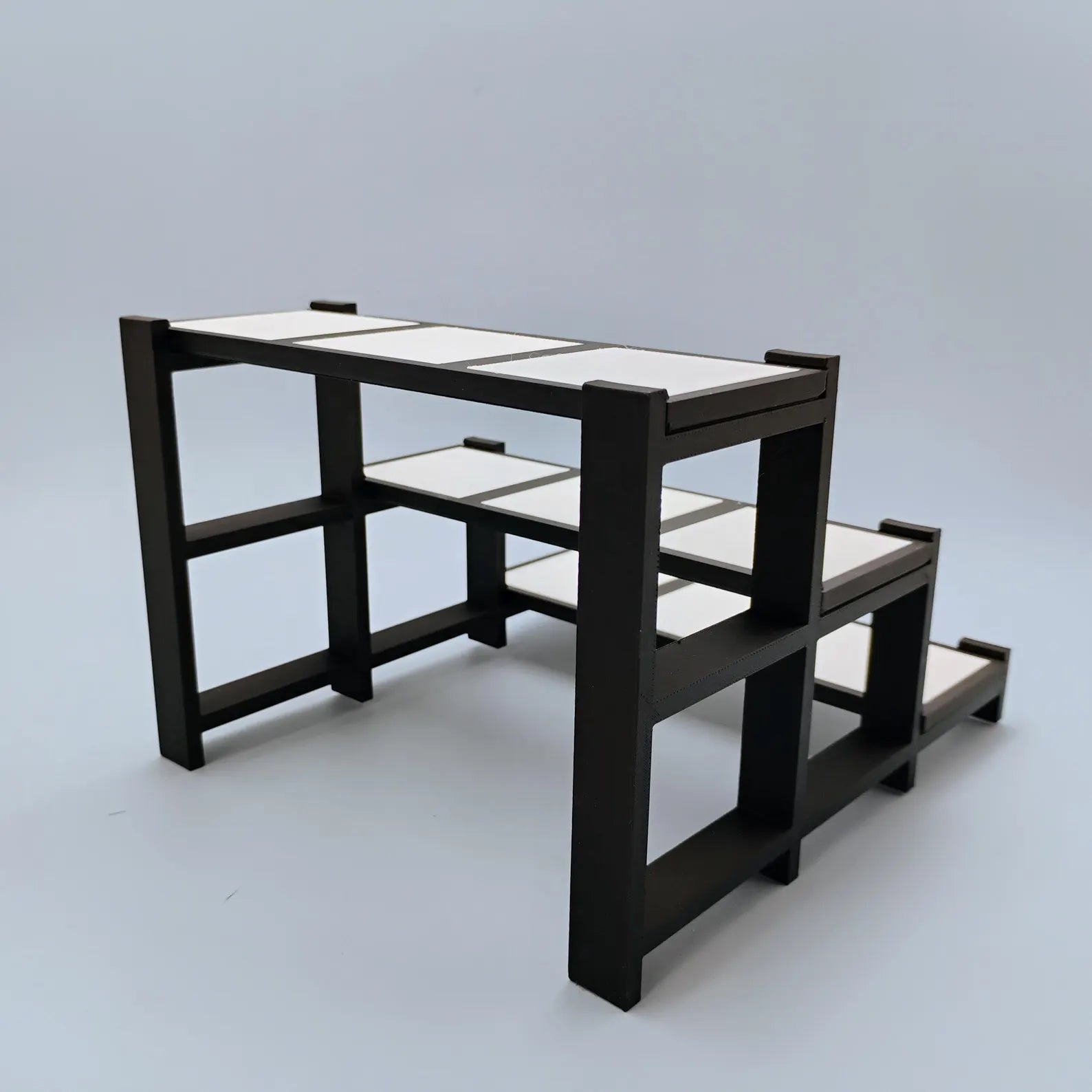 Side view of a black tiered display stand showing stepped shelves and removable tile spaces for collectibles and figures.
