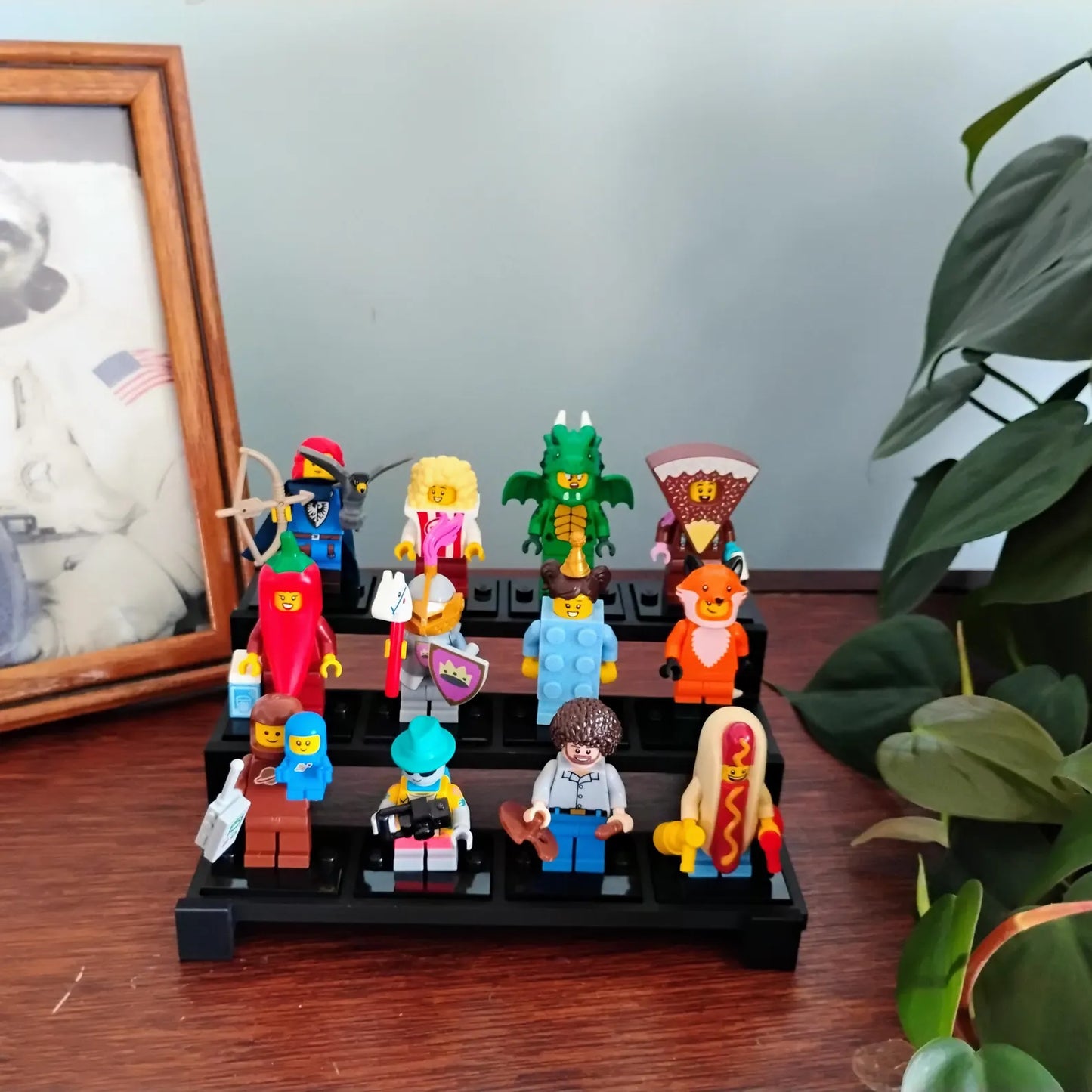 Tiered LEGO® minifigure display stand shown on a shelf with a colorful collection of figures.