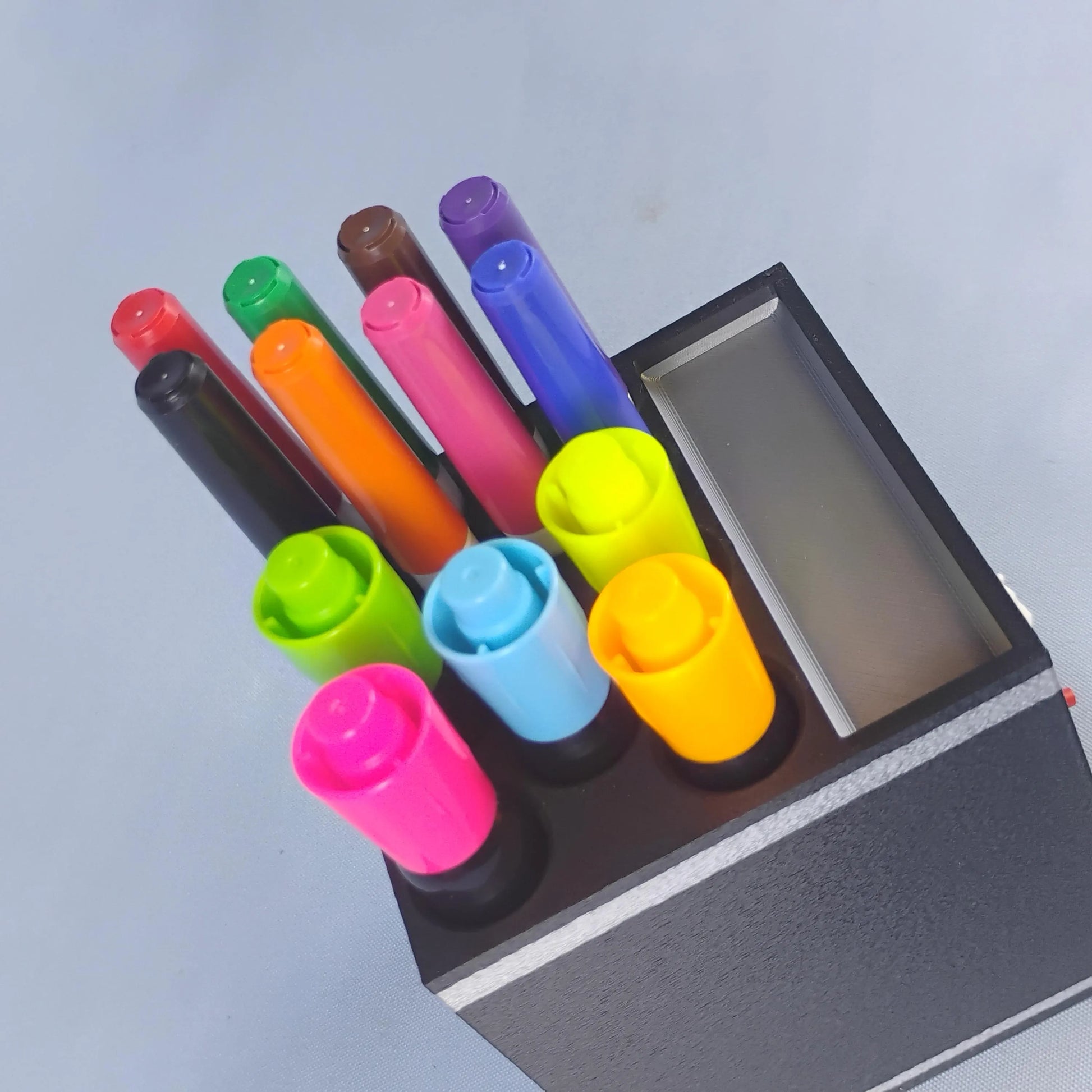 Top view of a white dry erase marker holder filled with colorful large and fine-tip Expo-style markers, showing the tiered storage layout and top tray.
