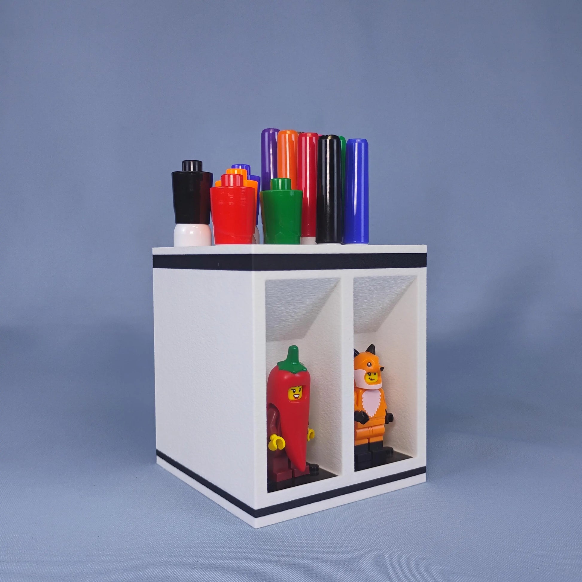 Angled front view of a white dry erase marker organizer holding large and fine-tip markers with two LEGO® minifigures displayed below.