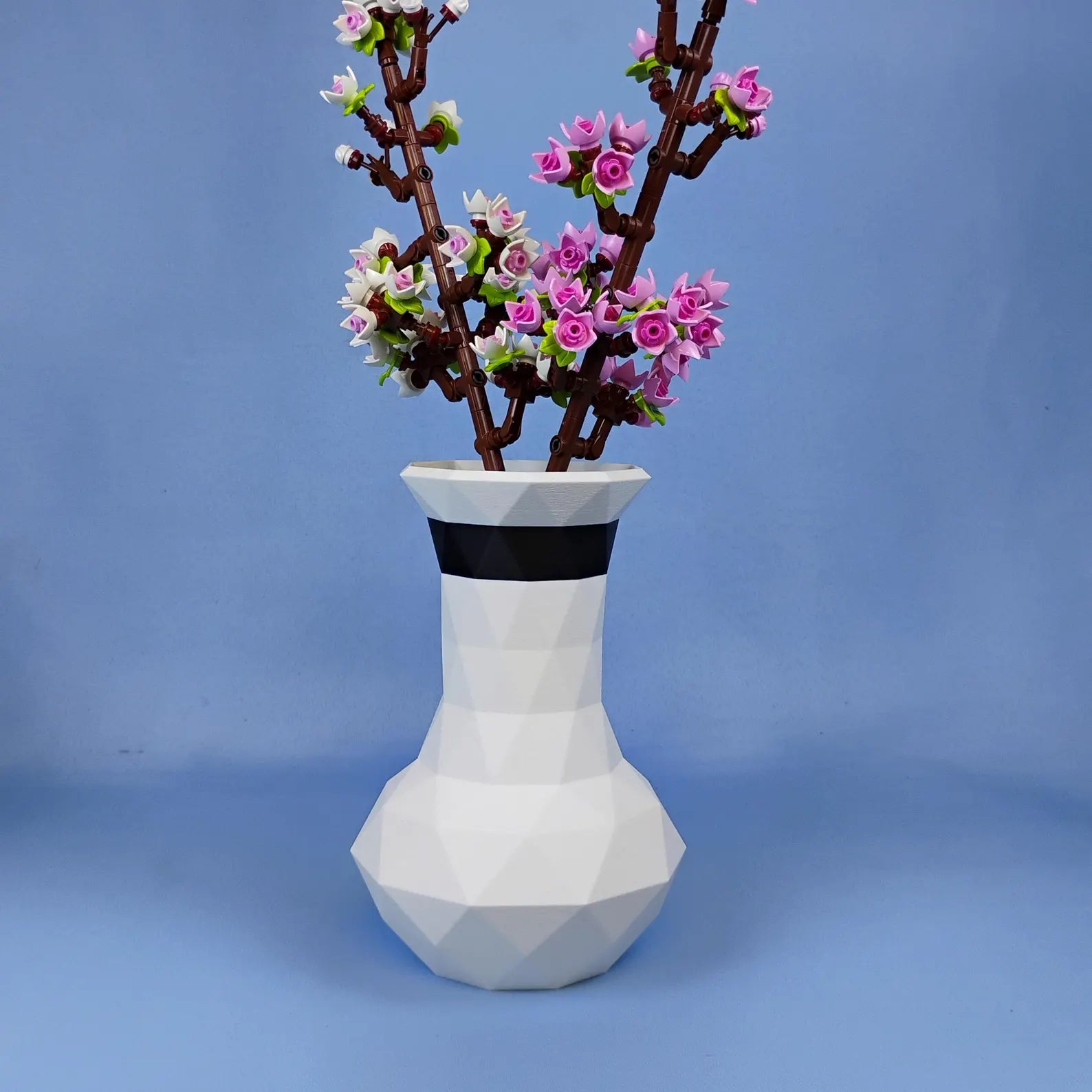 White geometric vase holding LEGO® cherry blossoms on a blue background