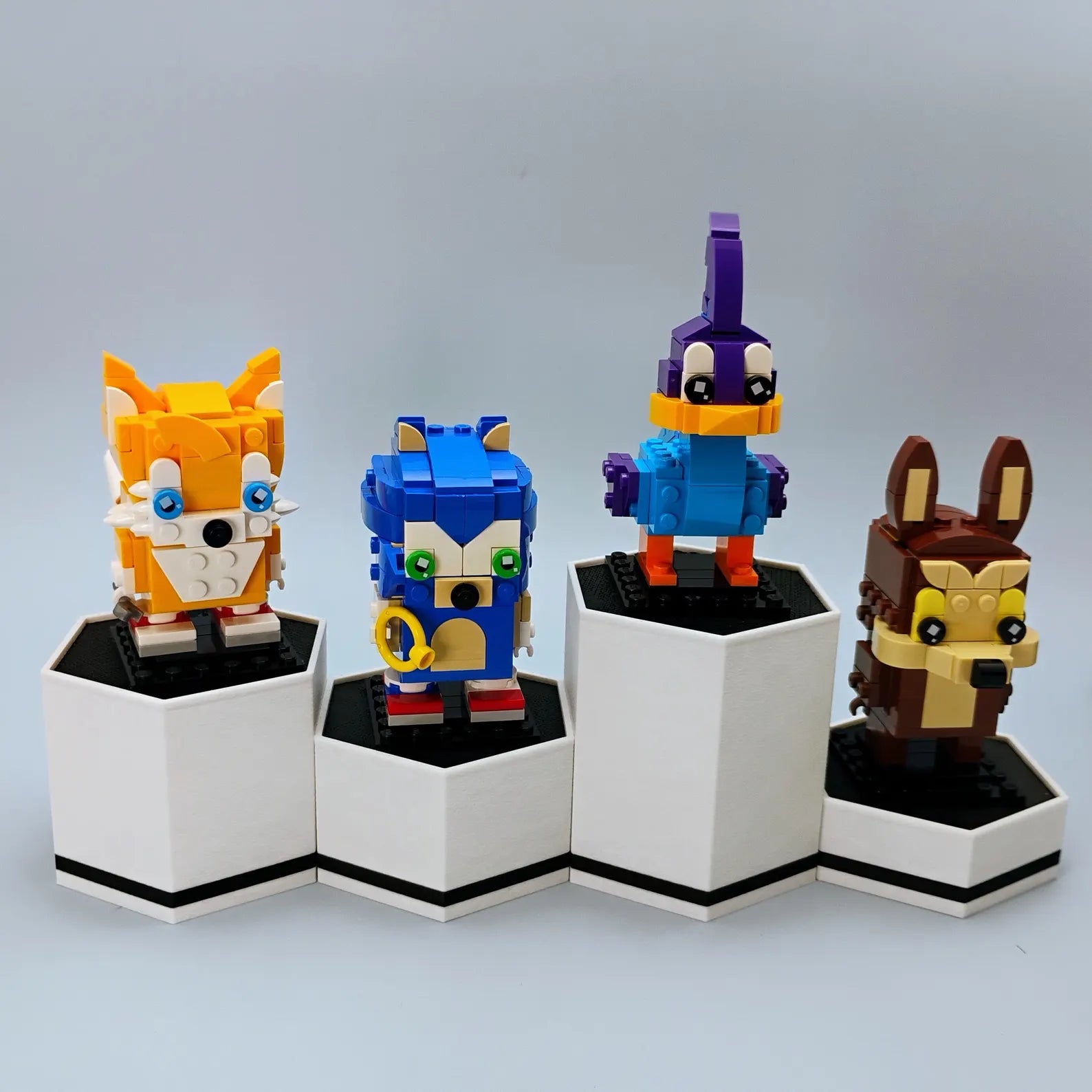 White hex display stands with black accents shown holding LEGO® BrickHeadz-style figures at different heights.