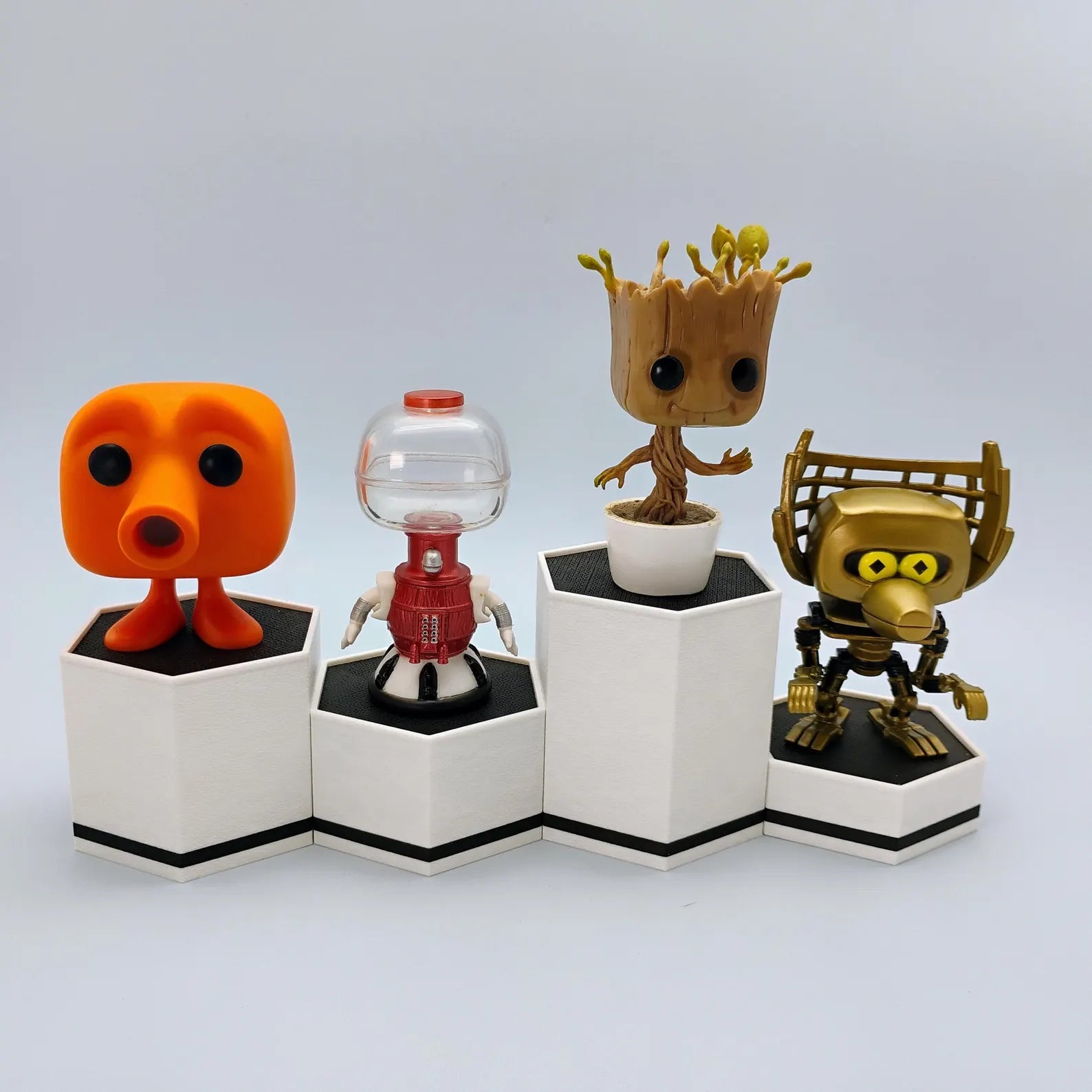 White hex display stands with black accents shown holding small collectible figures in a clean tiered arrangement.