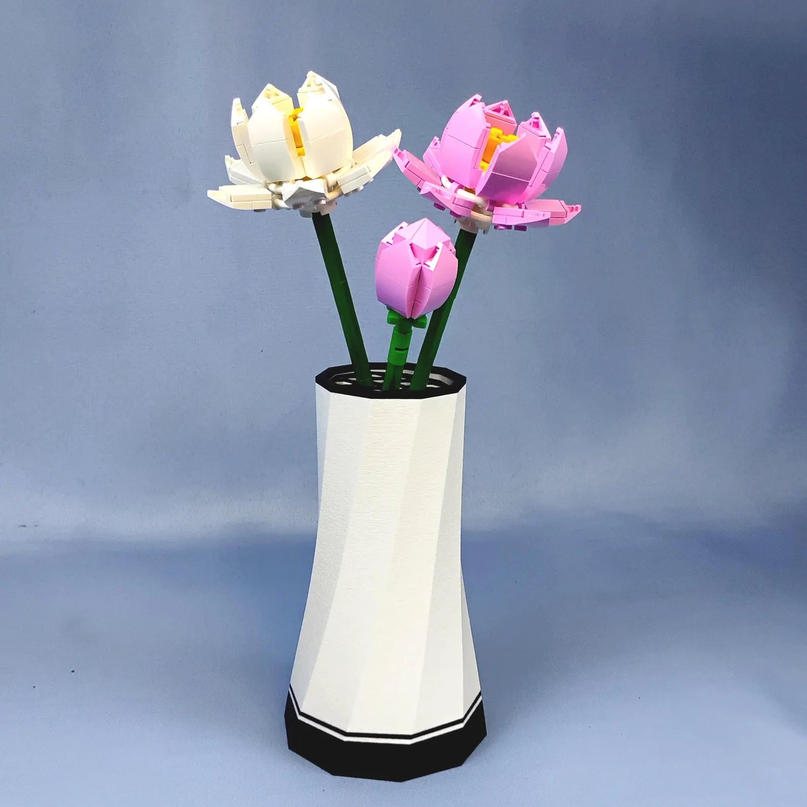 White faceted vase holding LEGO® Botanical lotus flower stems with black accent detail, designed for modern desktop or shelf display.