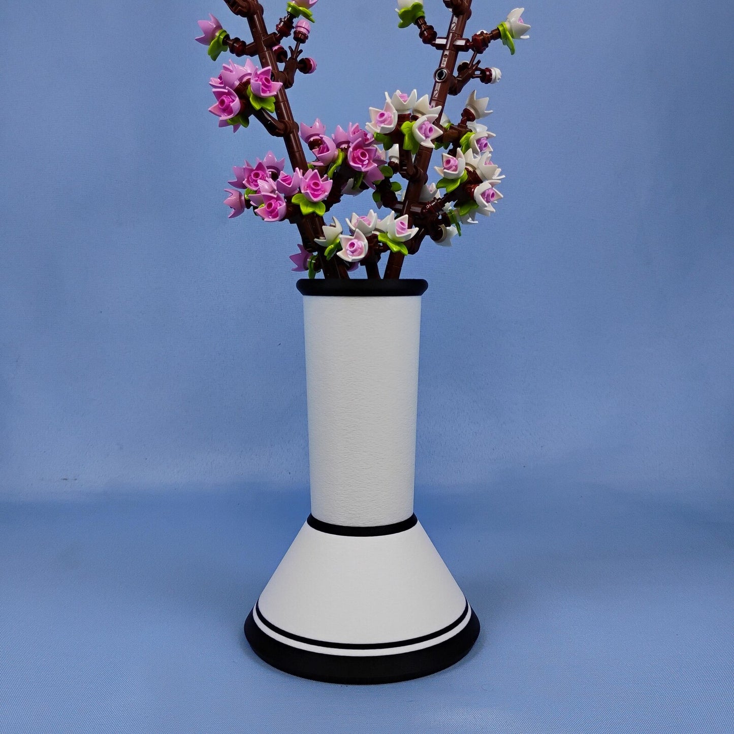 White minimalist vase holding LEGO® cherry blossoms on a blue background