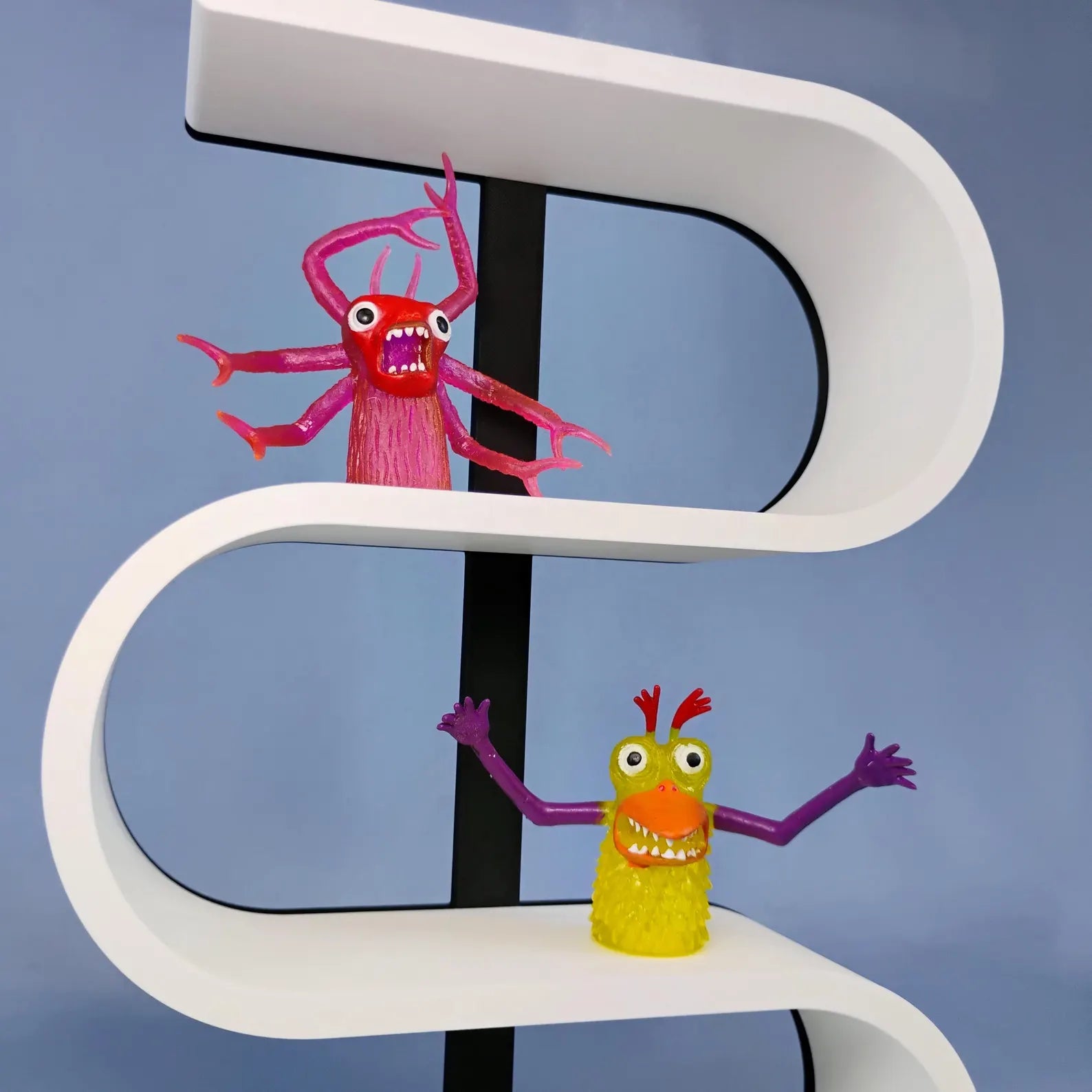Close-up of a white squiggly display shelf with a black center support, showing colorful miniature monster figures arranged on the curved display levels.