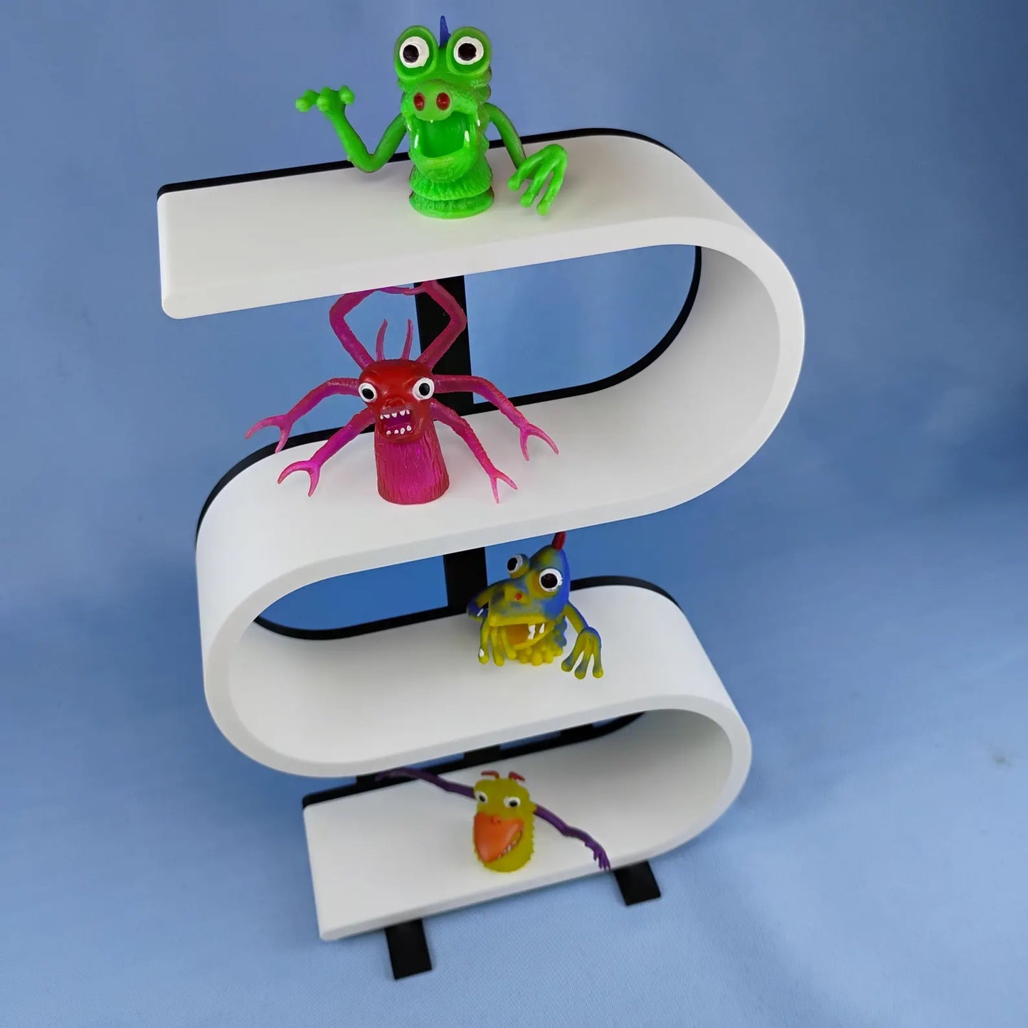 White squiggly display shelf with a black center support and removable feet, styled with colorful miniature monster figures across three curved display levels.