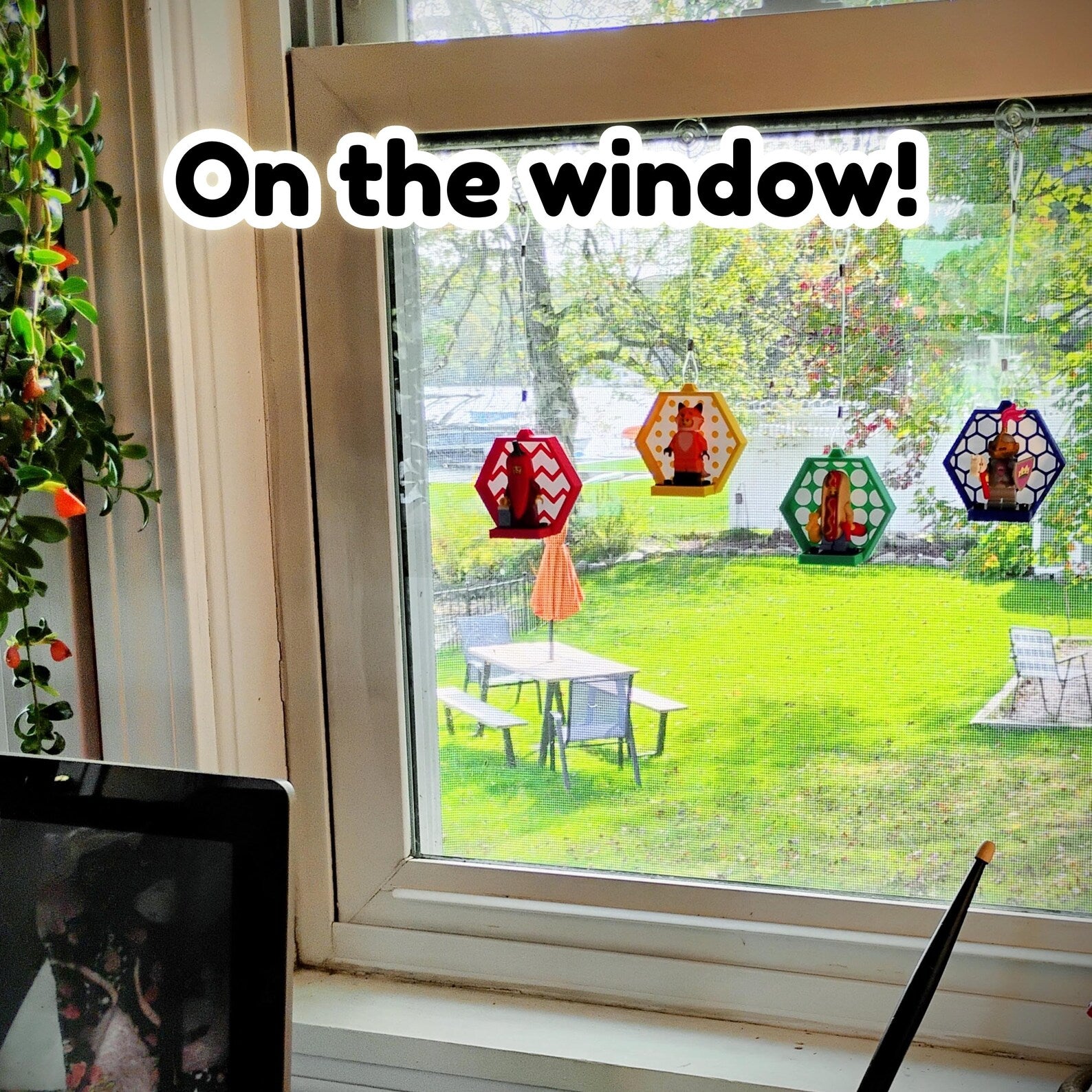 LEGO® minifigure displays hanging on a window with colorful frames, patterned backgrounds, and suction cup mounting lines.